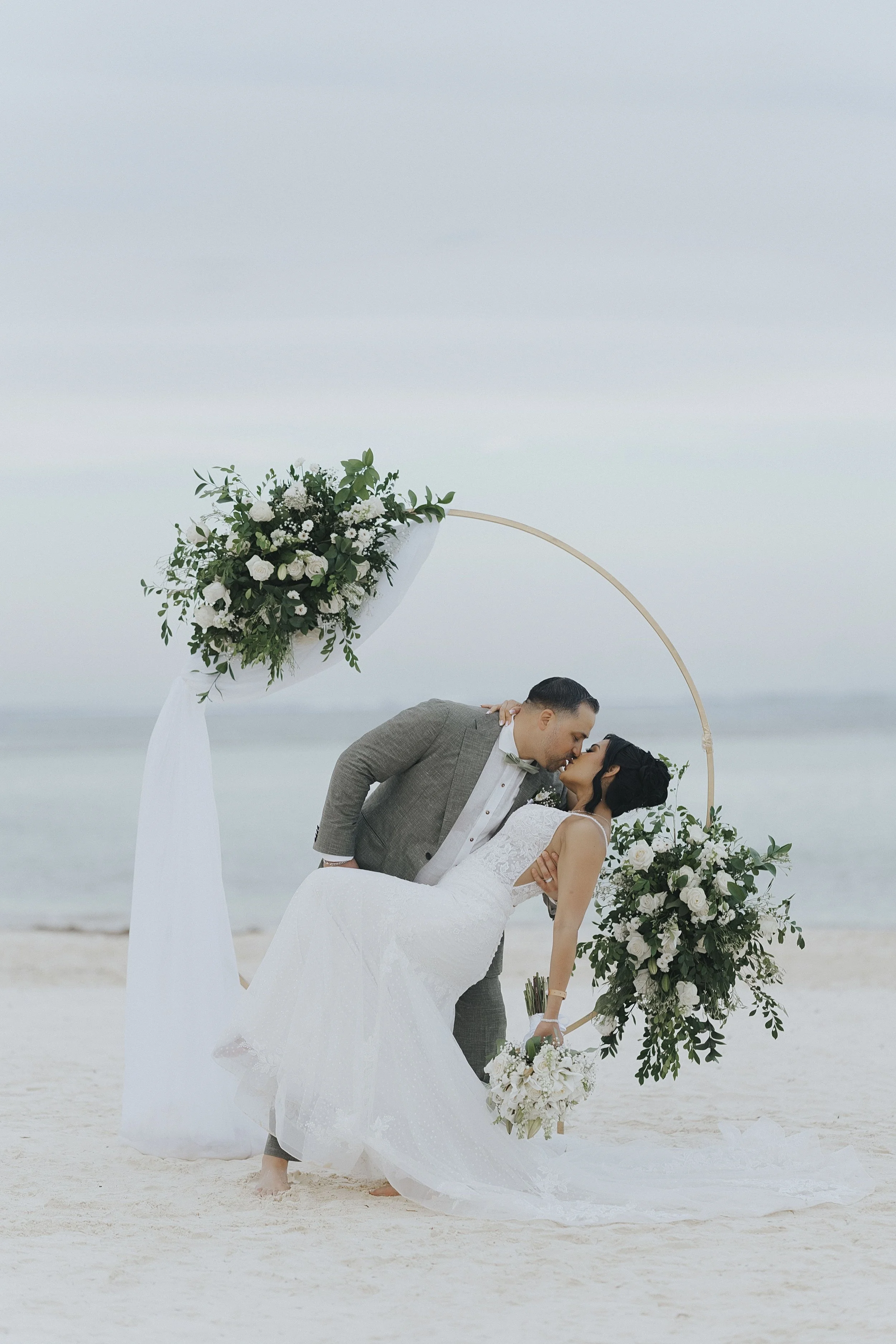 Groom dips bride for a kiss under the gold hoop arch during portraits. 