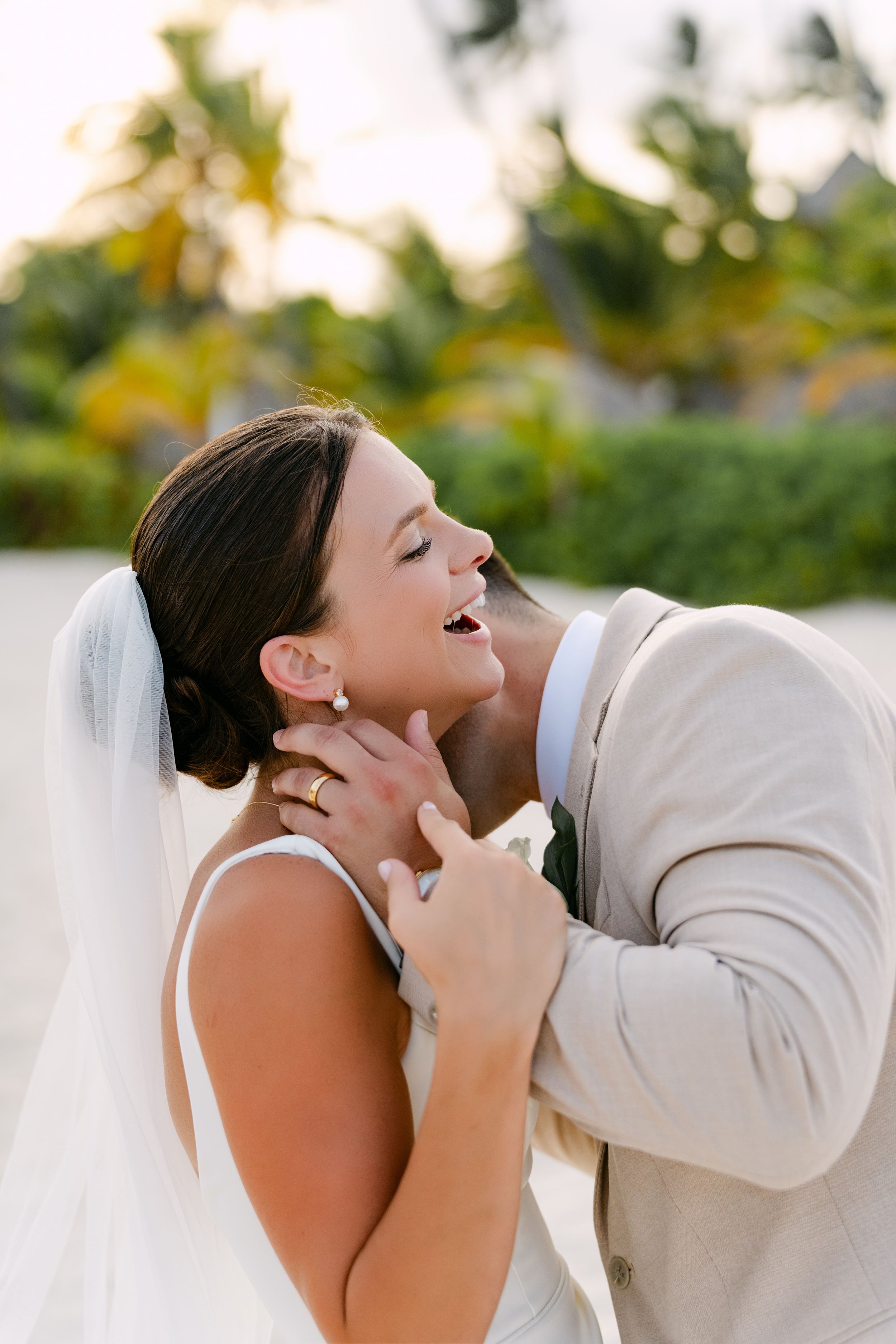 Bride laughing as groom holds her face, candid moment at Dreams Royal Beach Punta Cana wedding.