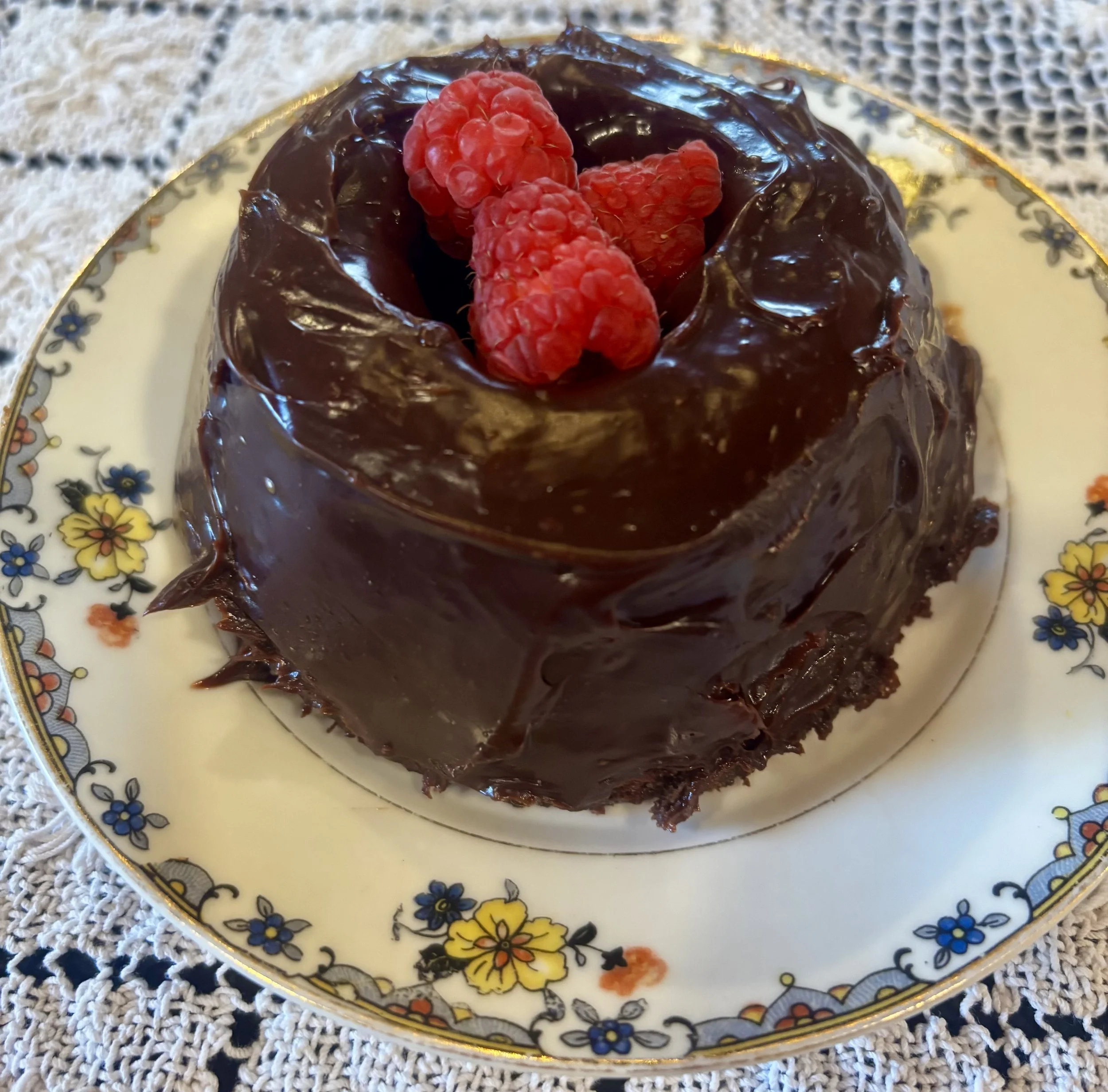 Mini chocolate bundt cake frosted with ganache and garnished with fresh raspberries.