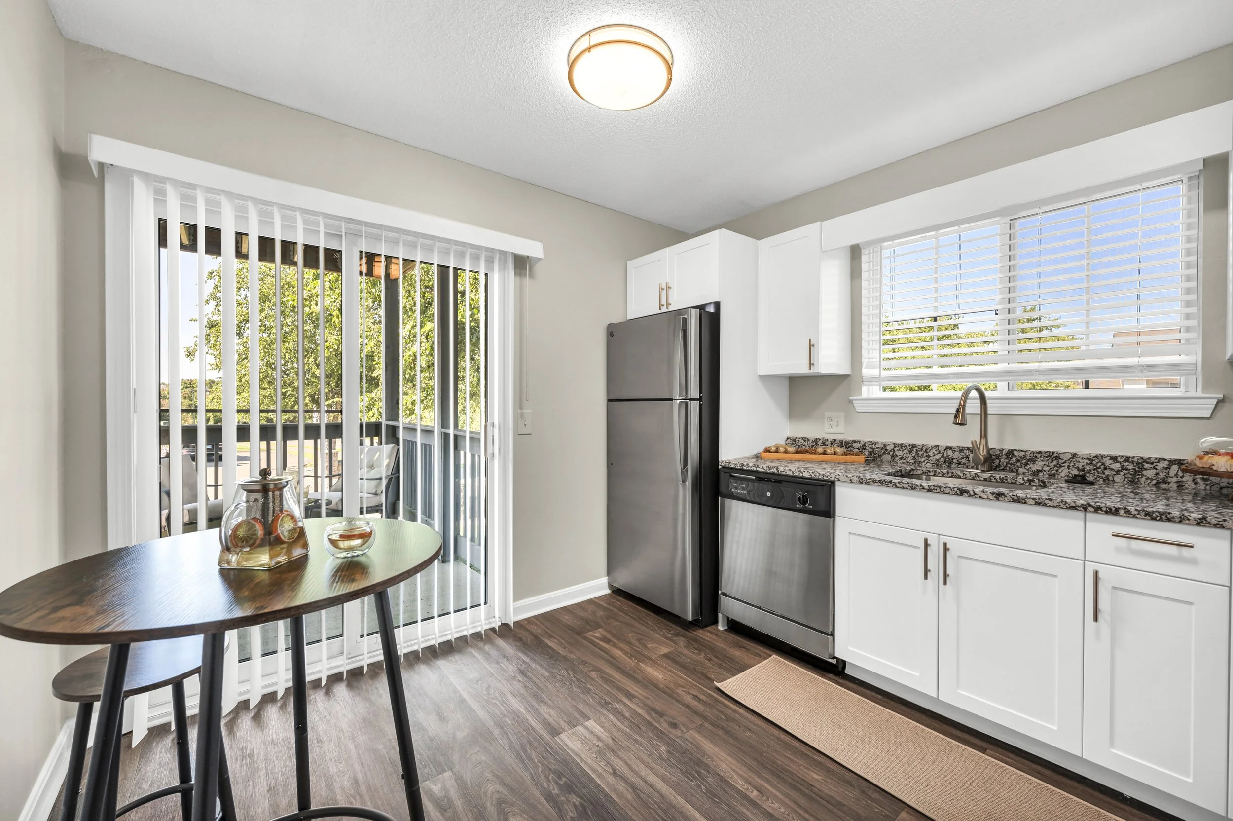 Modern apartment kitchen with white cabinets, stainless steel appliances, wood-style flooring, and a sliding glass door leading to a private patio.