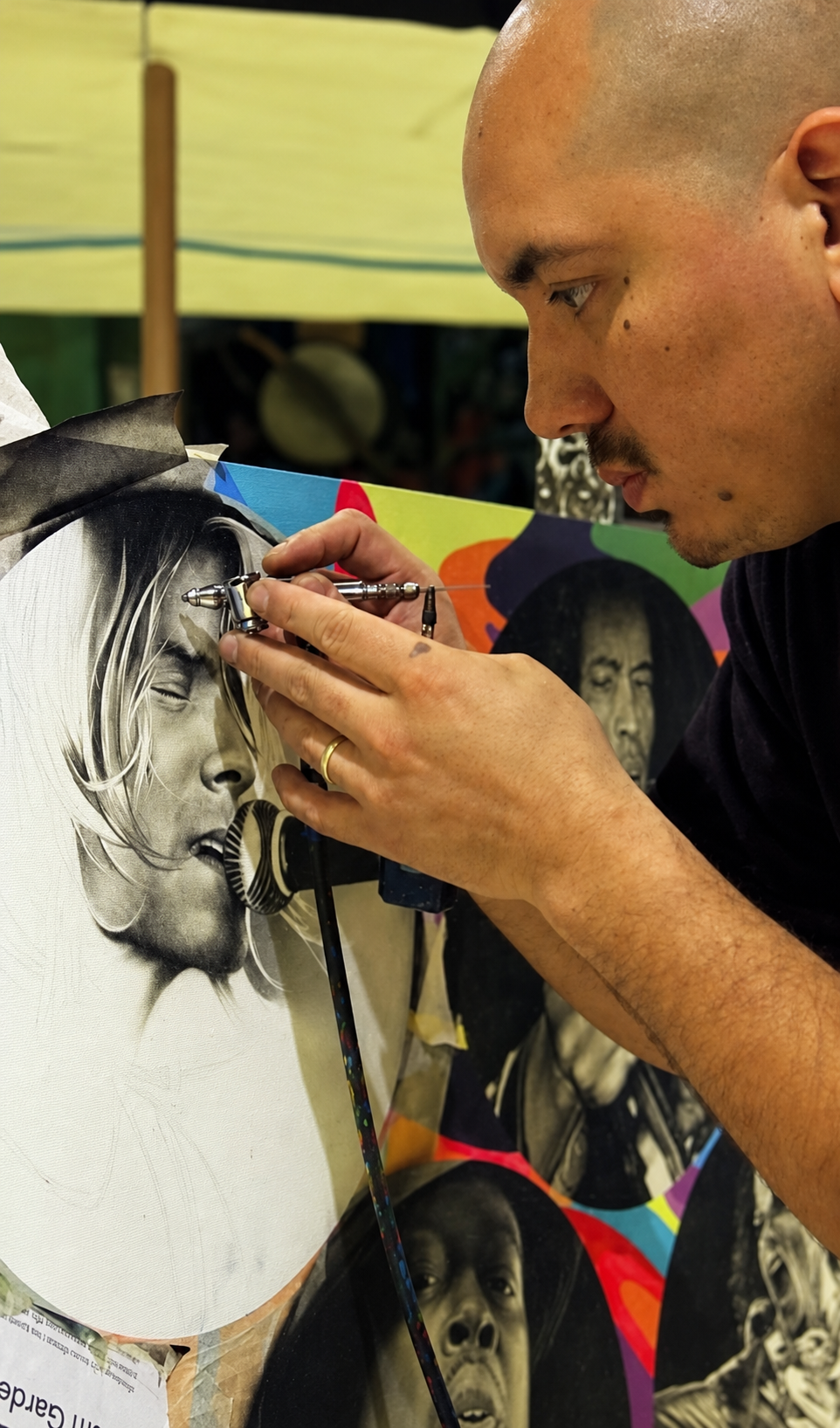 Eli Vallejo airbrushing a detailed black-and-white acrylic portrait on canvas.