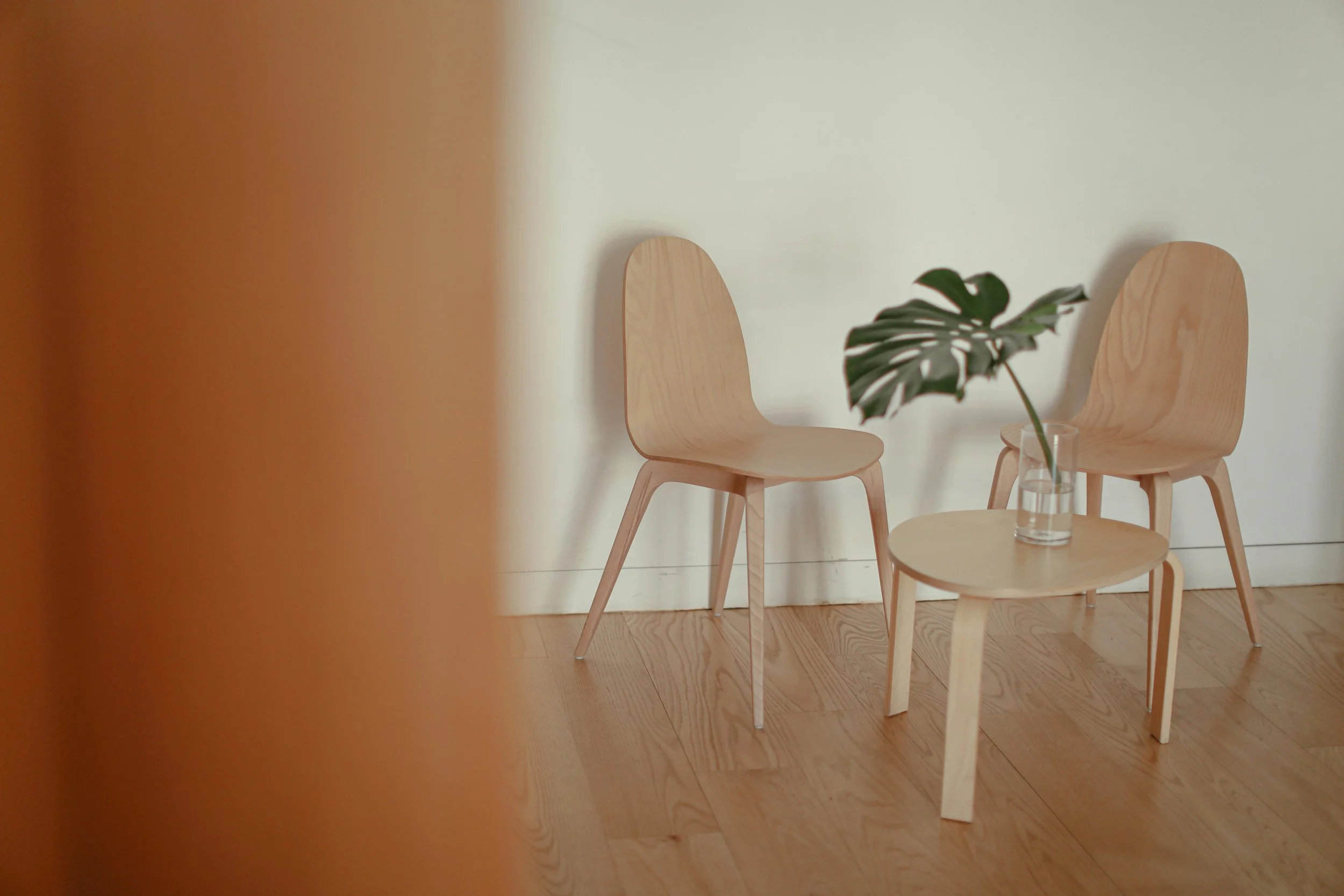 Due sedie di legno e un tavolino con un vaso di vetro con una pianta verde, in un ambiente con pareti chiare e pavimento in legno