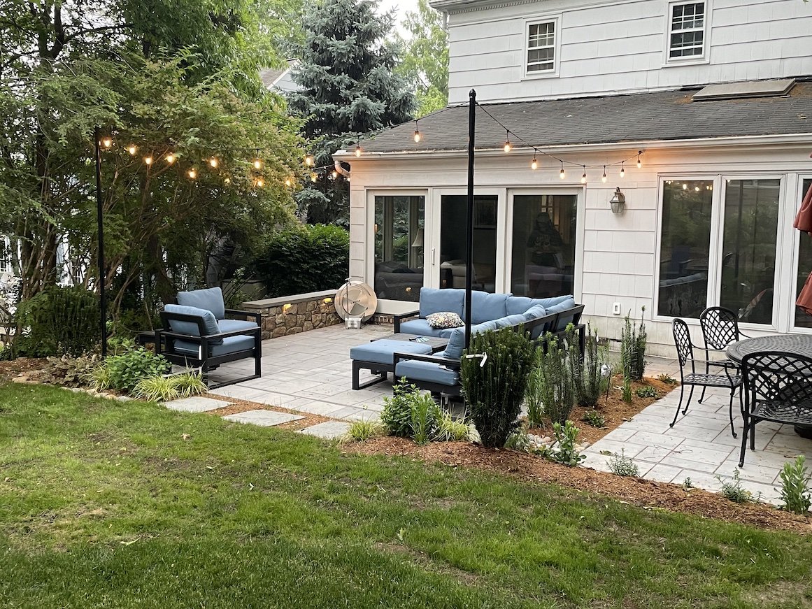 Backyard patio area with italian string lights, blue couches, black metal accents and stepping stones with a yard.jpg