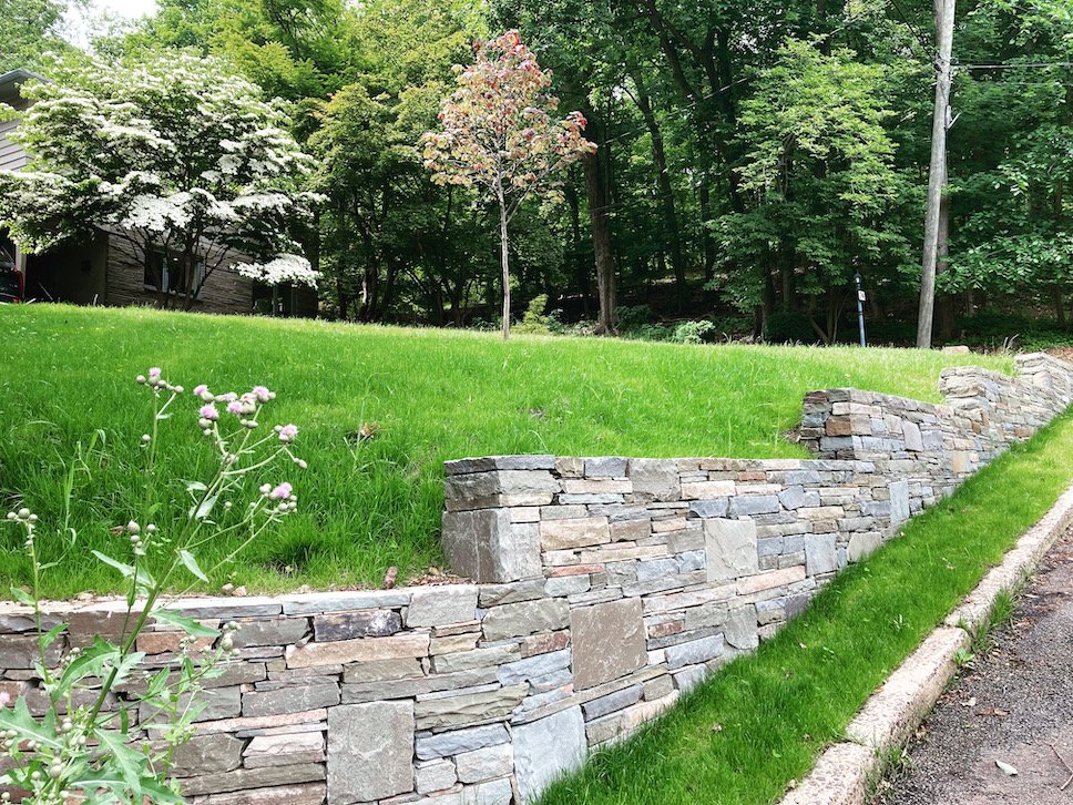Natural stone retaining wall surrounded by trees and green grass.JPEG