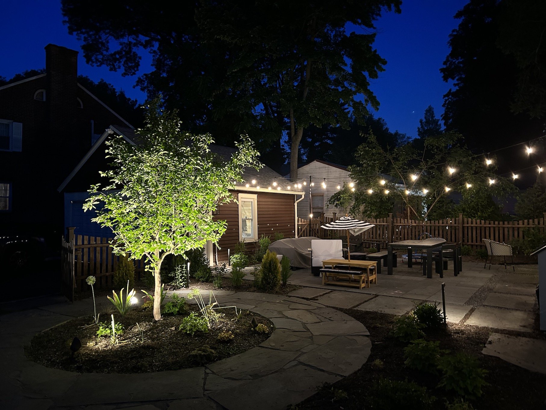Landscape lighting with string lights on outdoor patio surrounded by trees and picnic furniture.jpg