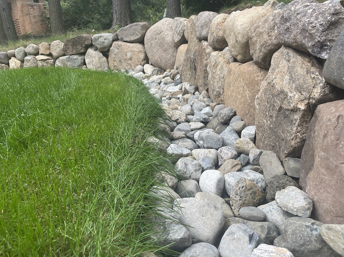 Drainage disguised by natural river rocks along outer perimiter landscaping of home in northern nj.JPEG