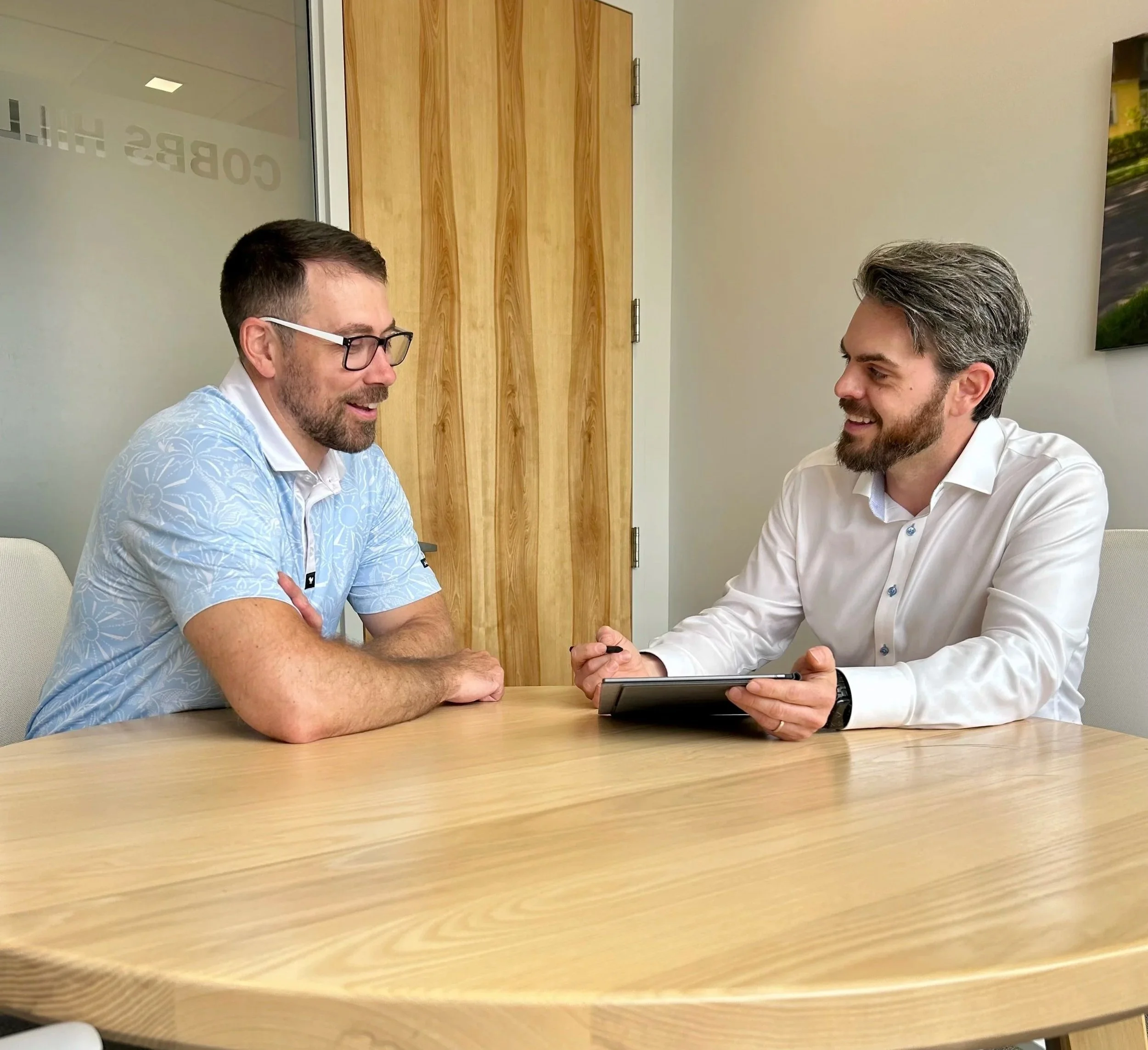 Two men sitting at a table looking at a notebook in conversation