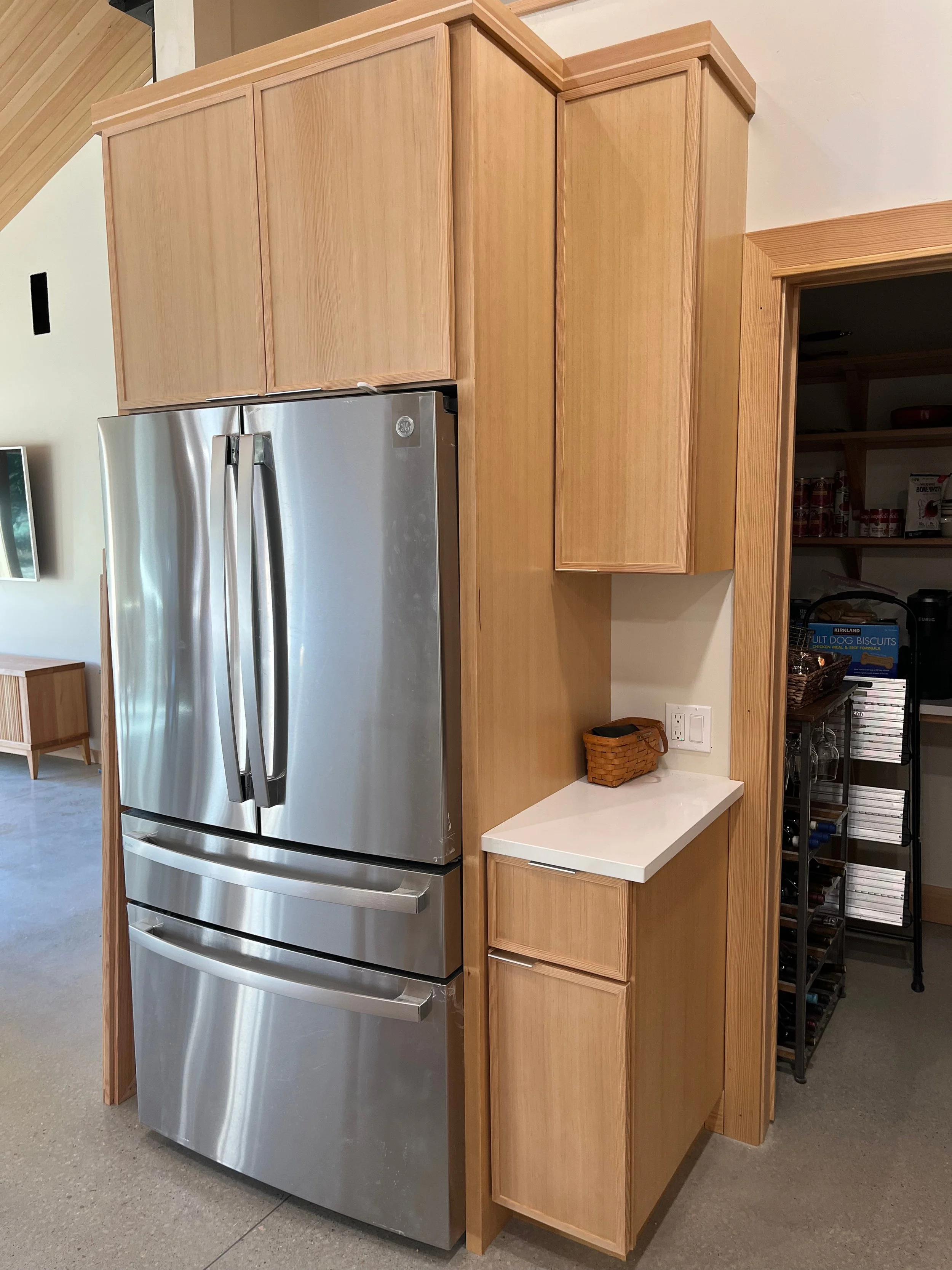 Kitchen with wooden cabinets and stainless steel refrigerator, corner space with open shelves containing canned goods and kitchen appliances.