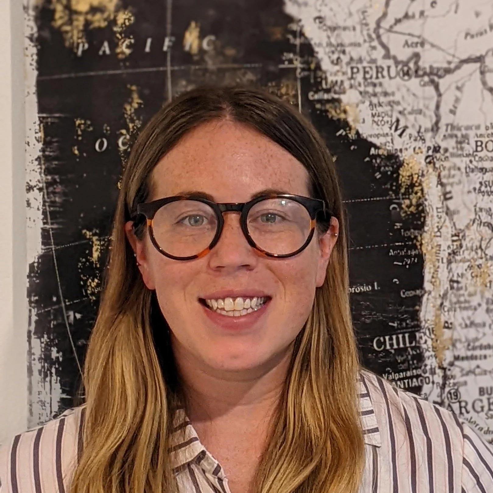 A woman with long brown hair, glasses, and a striped shirt smiling at the camera.