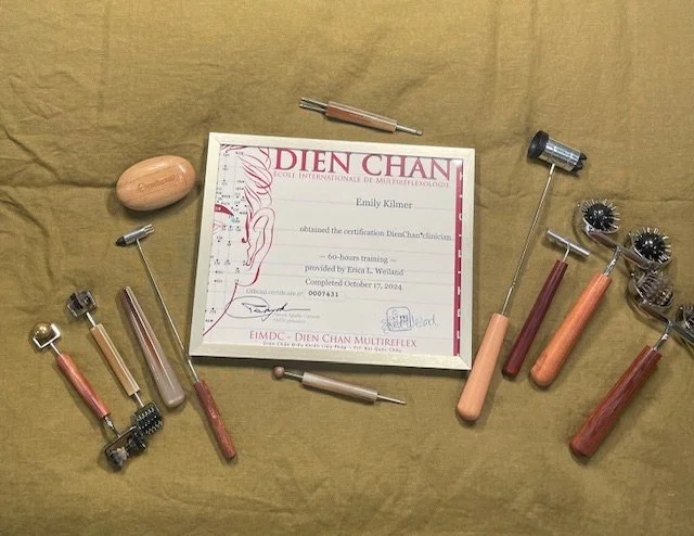 A certificate of completion for the Dien Chan facial reflexology technique, surrounded by various metal and wooden tools and rollers used for facial massage and therapy, placed on a yellow cloth background.