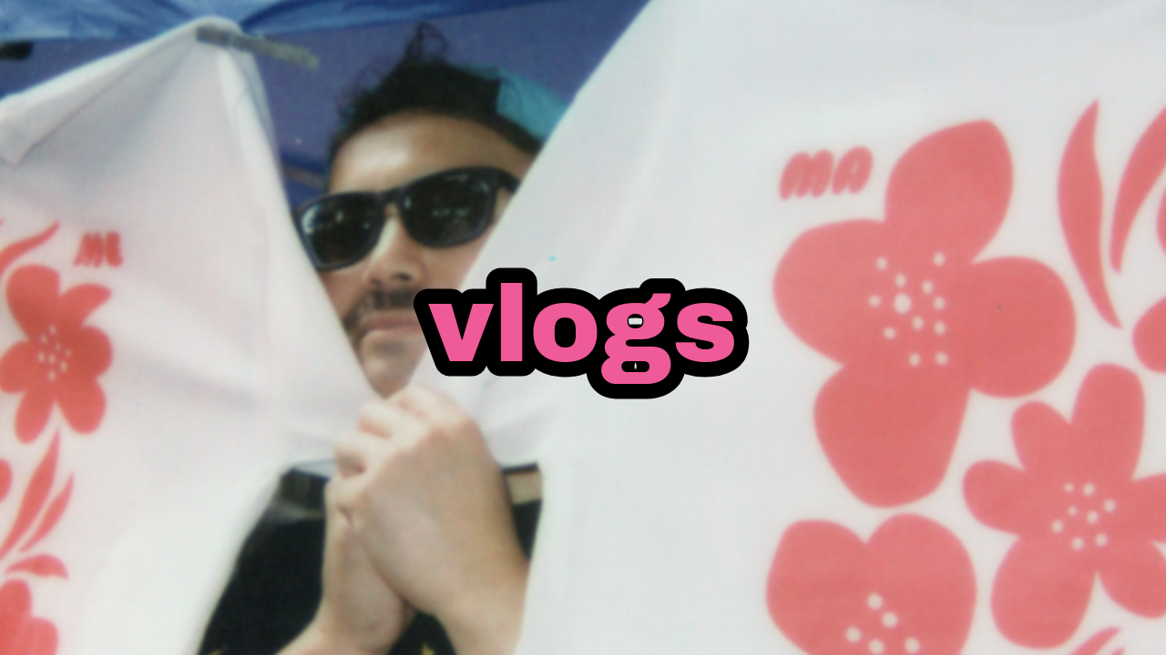 A person wearing sunglasses holding a large white and pink floral-patterned object with the word 'vlogs' overlaid in pink and black text.