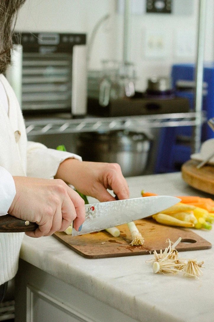 Person chopping vegetables, including carrots and white mushrooms, on a wooden cutting board in a professional kitchen.