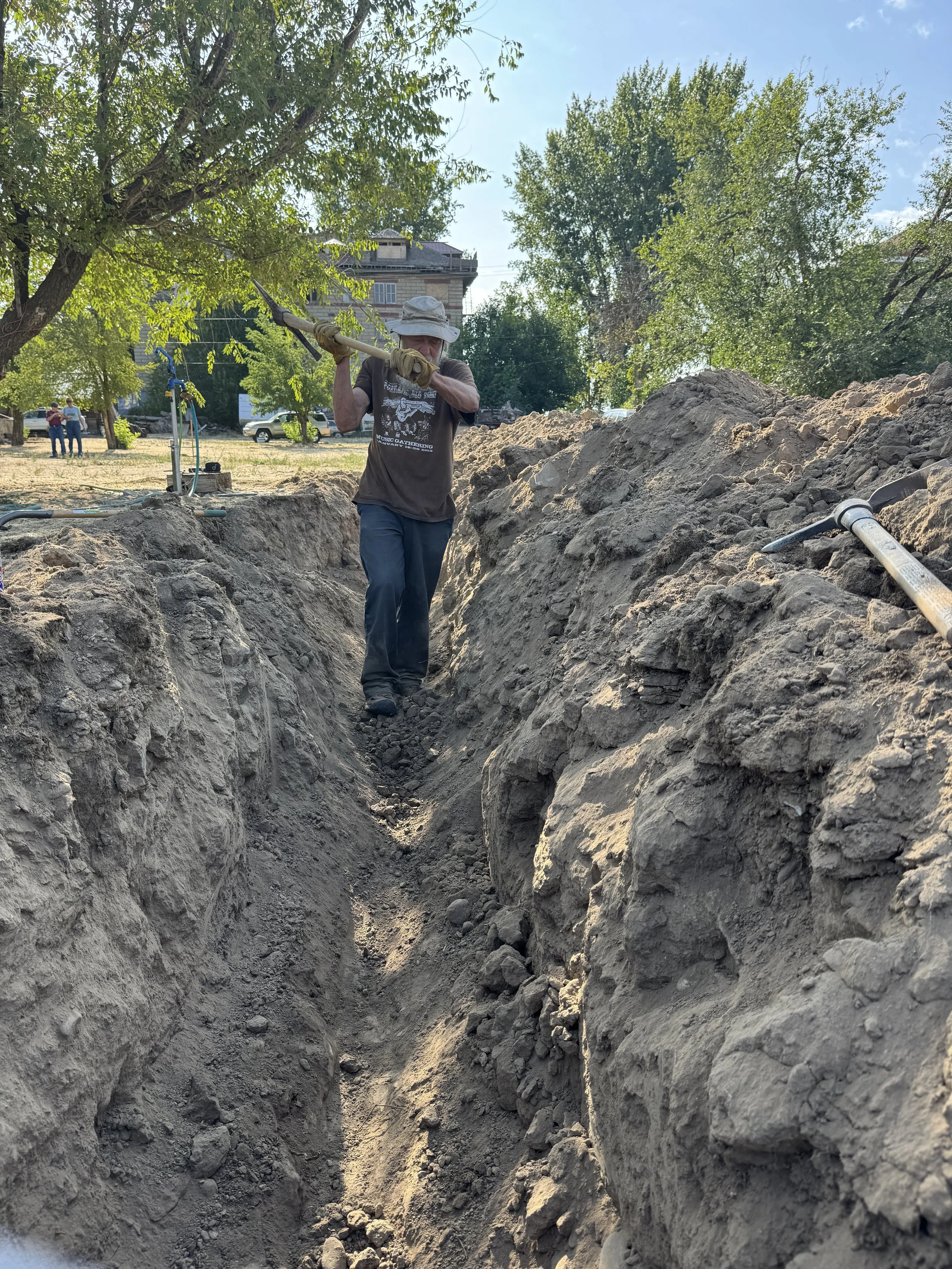 Dave Jensen (Fiddle) manually digging the trench for the water supply line. The mini-excavator could only dig so deep, but the waterline had to be buried below the frostline, so some manual digging was required. 