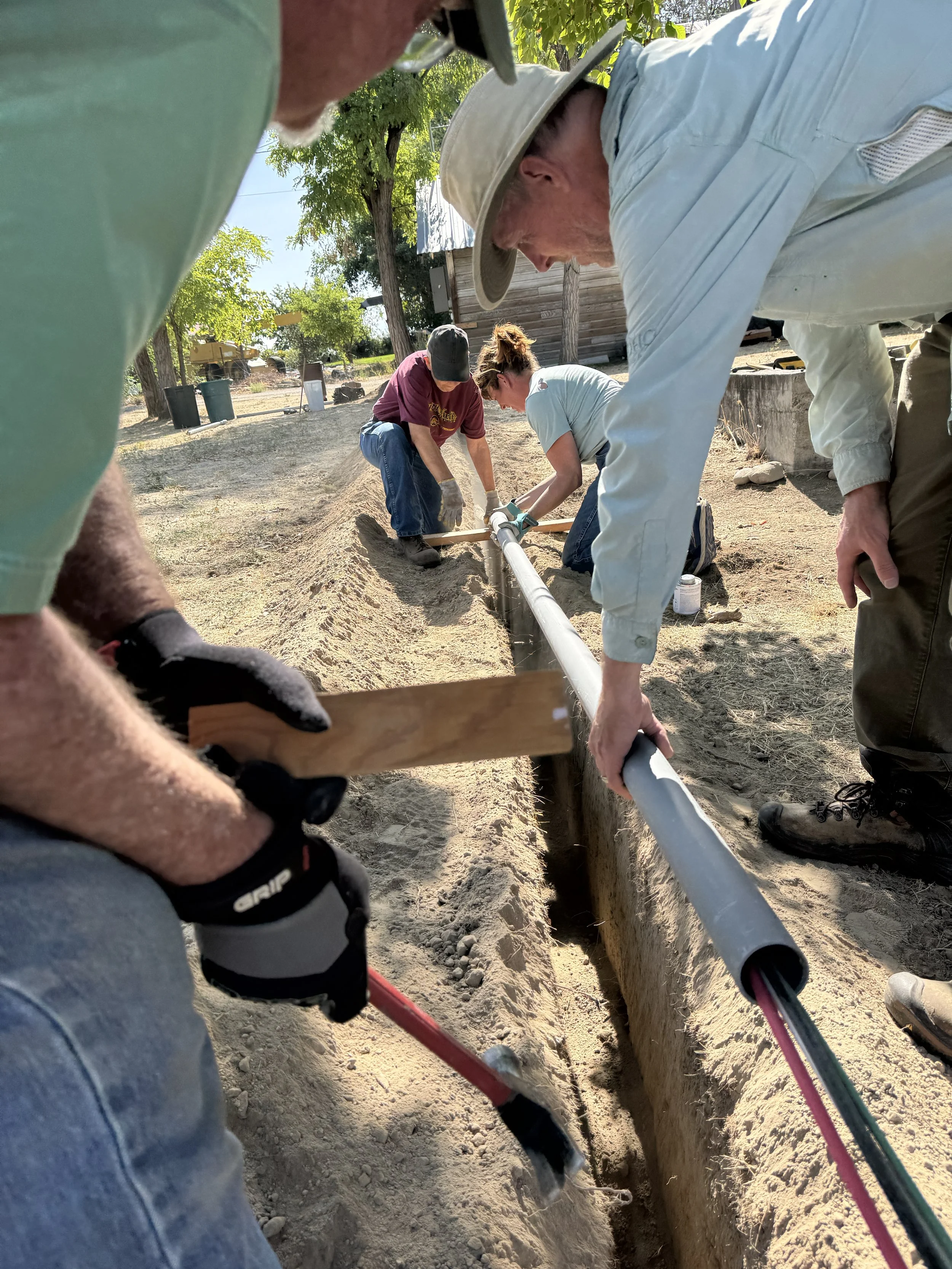 Volunteers Bill Siems (Mandolin), Marsha Schoeffler (Fiddle), Kate Little (Guitar) and Keith Walklet (Banjo) install the electrical line to the bathhouse build site. 


