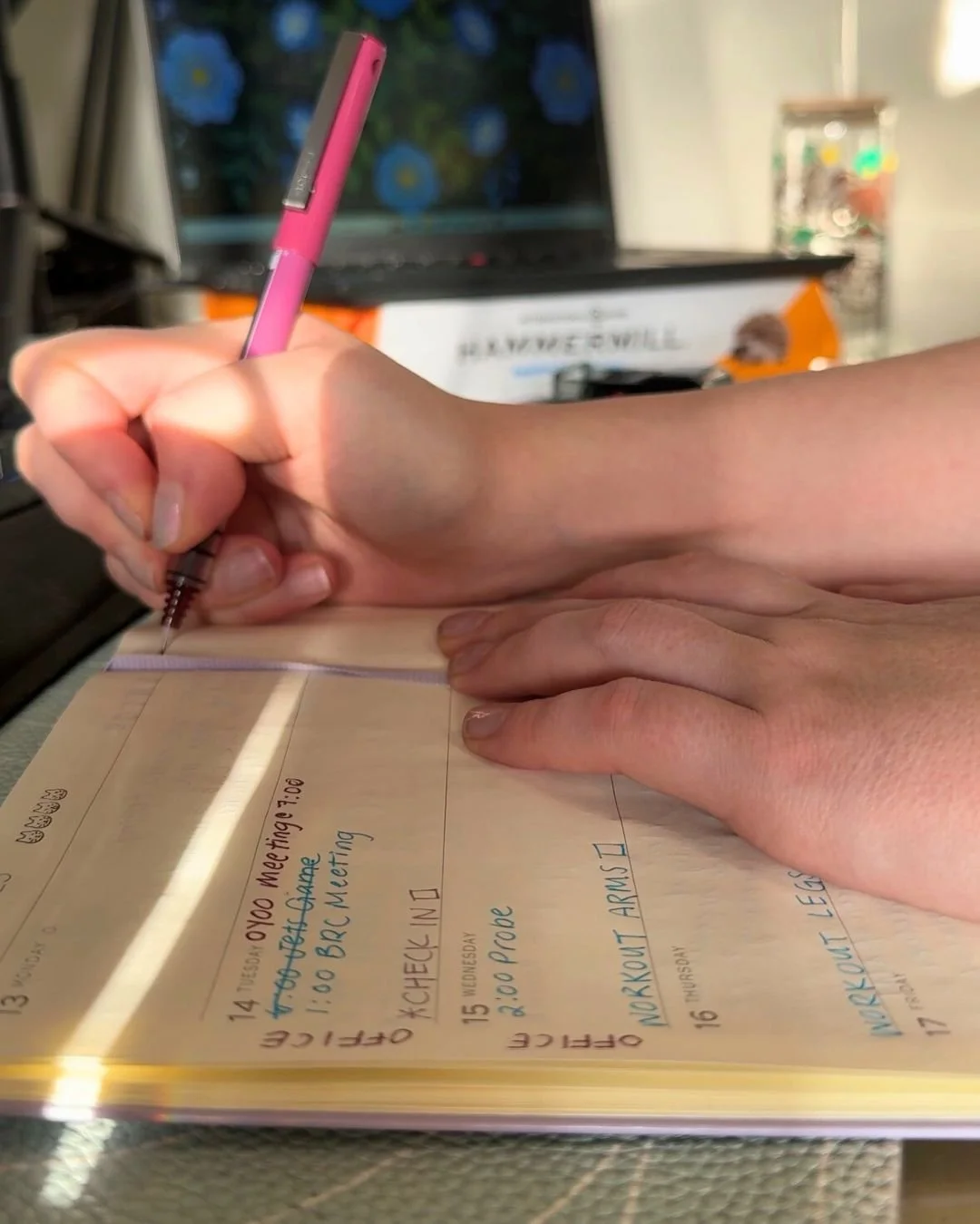 A caucasian woman's hands holding a pink pen, writing in a notebook.