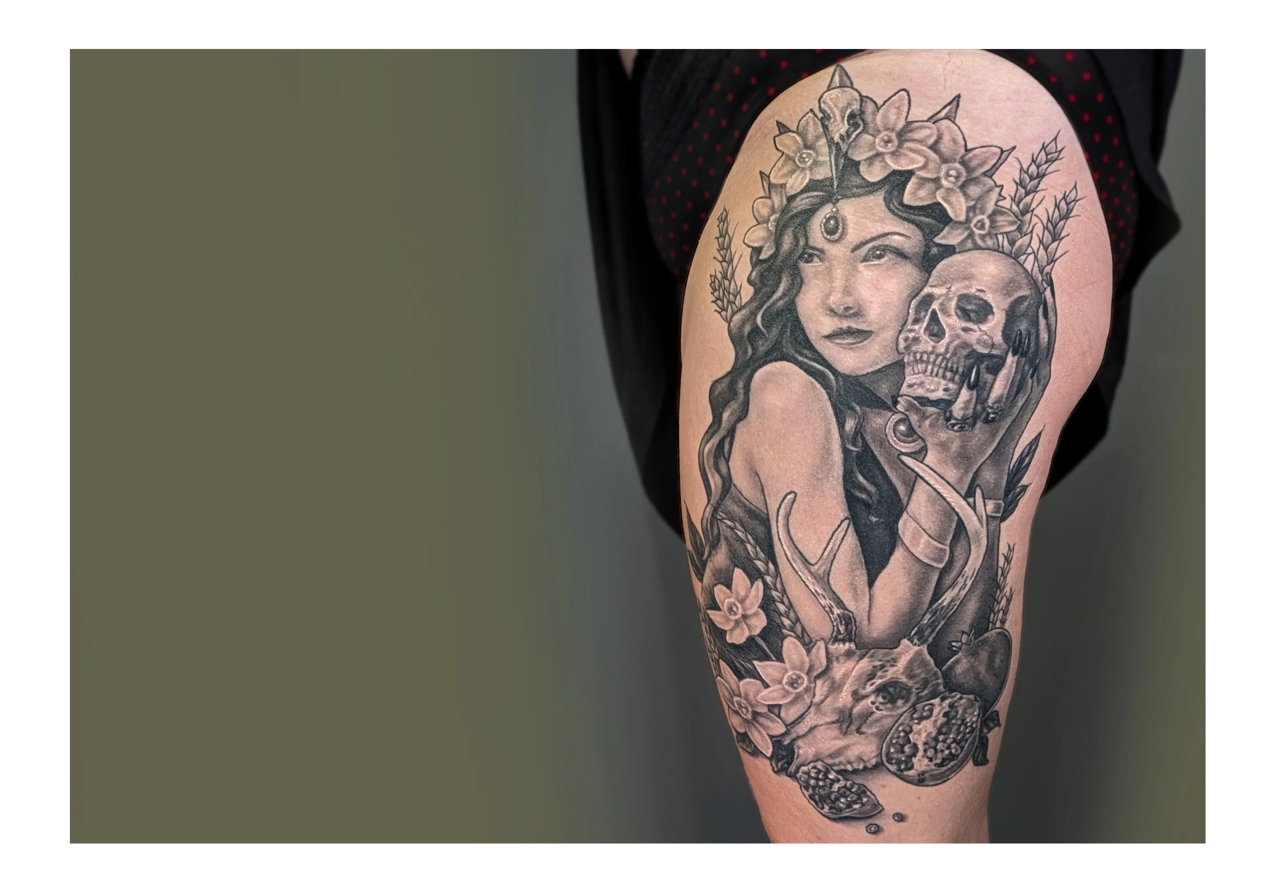 Tattoo of goddess Persephone holding a skull, wearing a crown of flowers, surrounded by wheat and animal skulls.  On a woman's upper thigh.