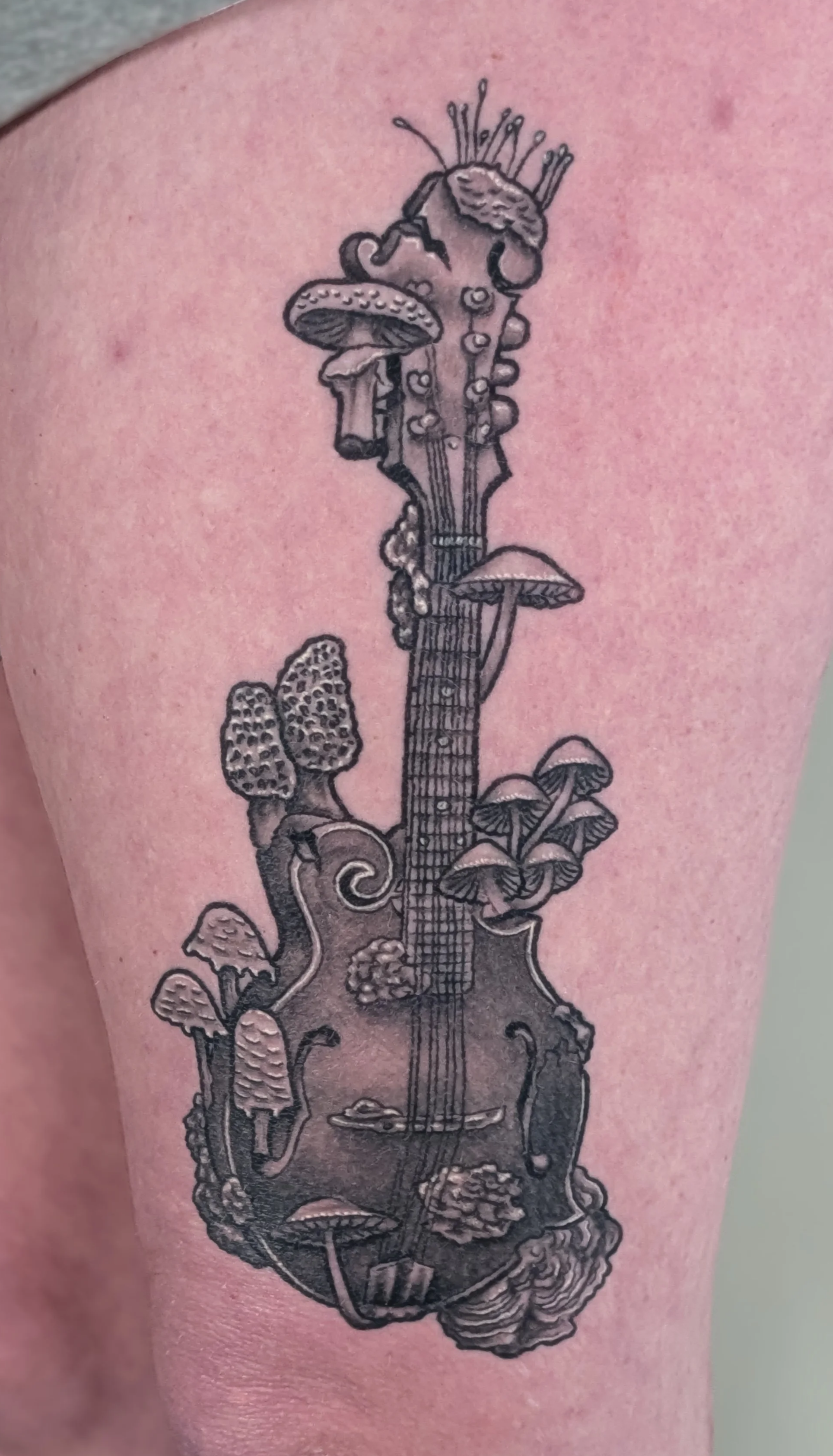 Black and gray tattoo of a guitar adorned with various mushrooms and fungi, with some growing along the neck and body.