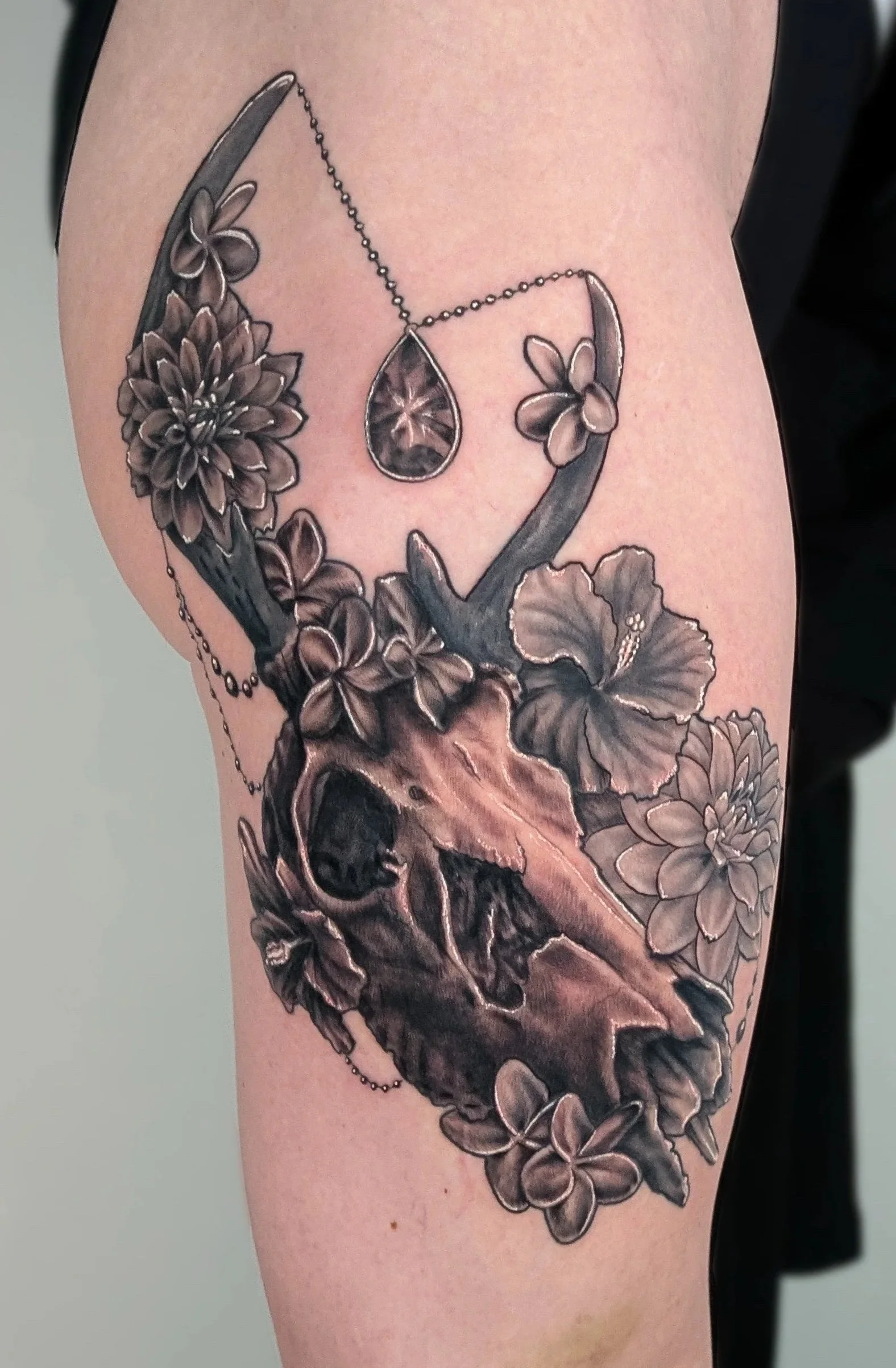 Black and gray tattoo of flowers, a skull, and a teardrop-shaped gem on a person's upper arm.