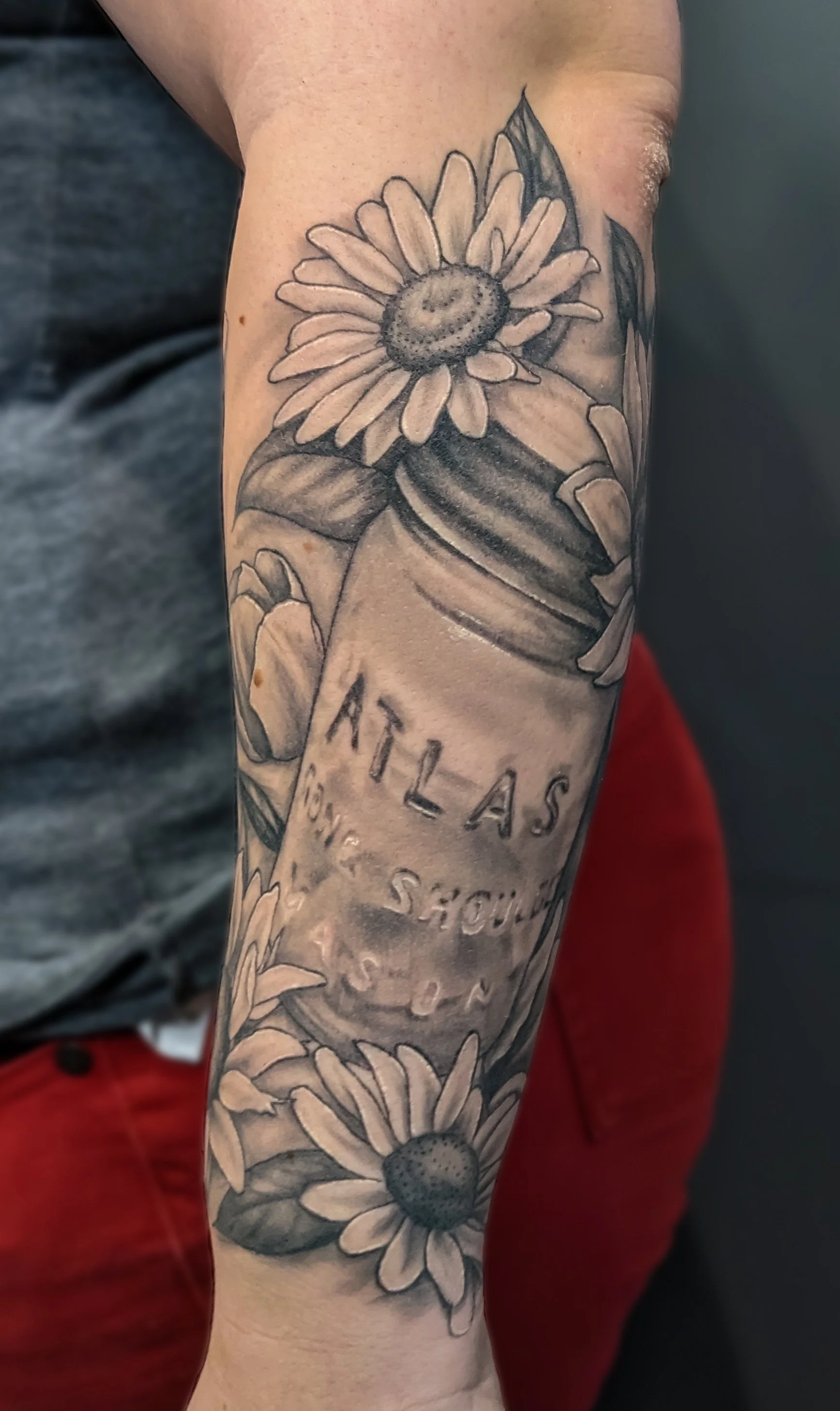 Black and gray floral tattoo on person's arm featuring daisy flowers and leaves.