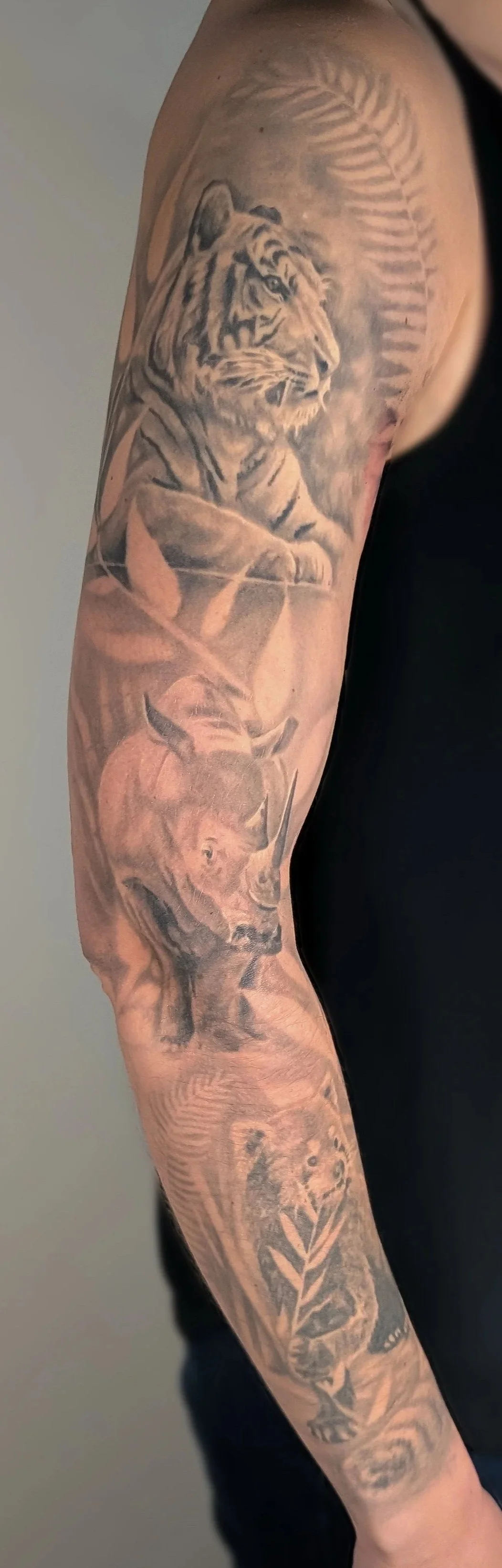 Tattoo sleeve featuring a tiger, a bear, a lion, a lioness, and a lion cub, with fern and leaf details.
