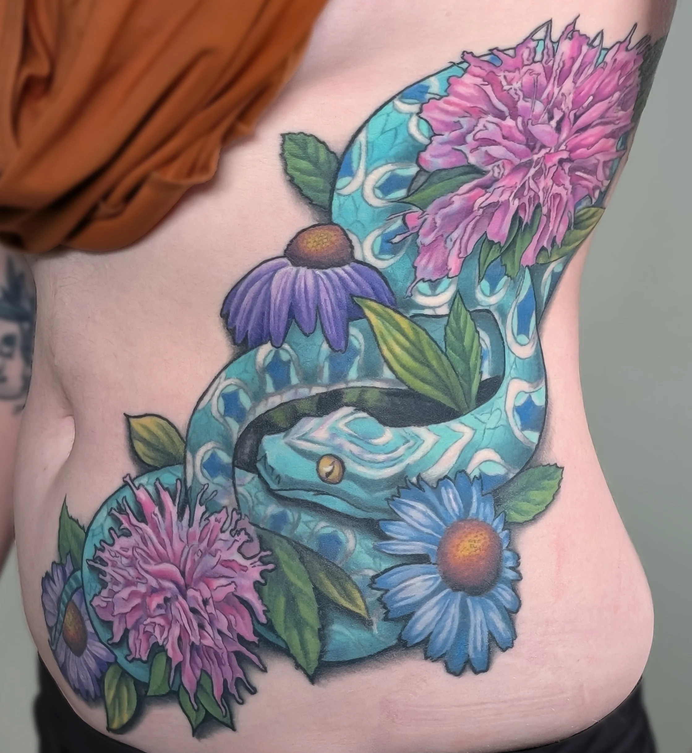Colorful tattoo of a butterfly and pink, purple, and blue flowers on someone's skin.