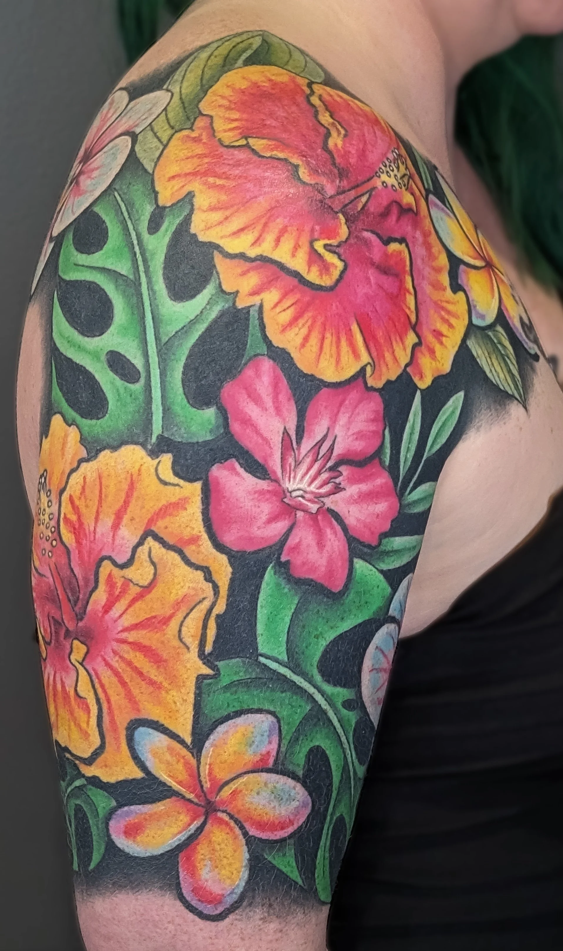 Colorful tattoo of tropical flowers and green leaves on person's upper arm.