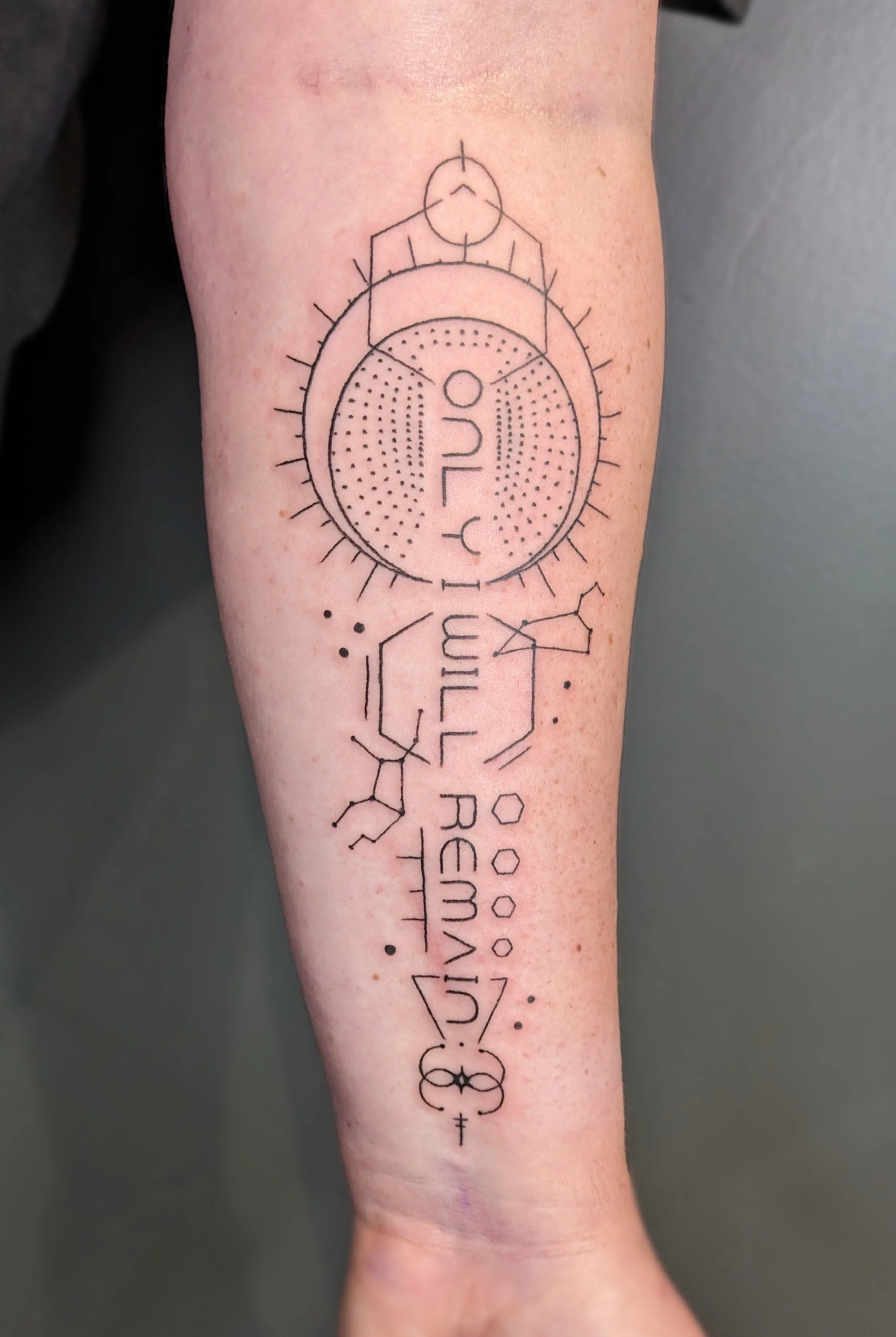 A geometric tattoo on a person's inner forearm featuring circles, lines, dots, and symbols arranged in an intricate pattern.