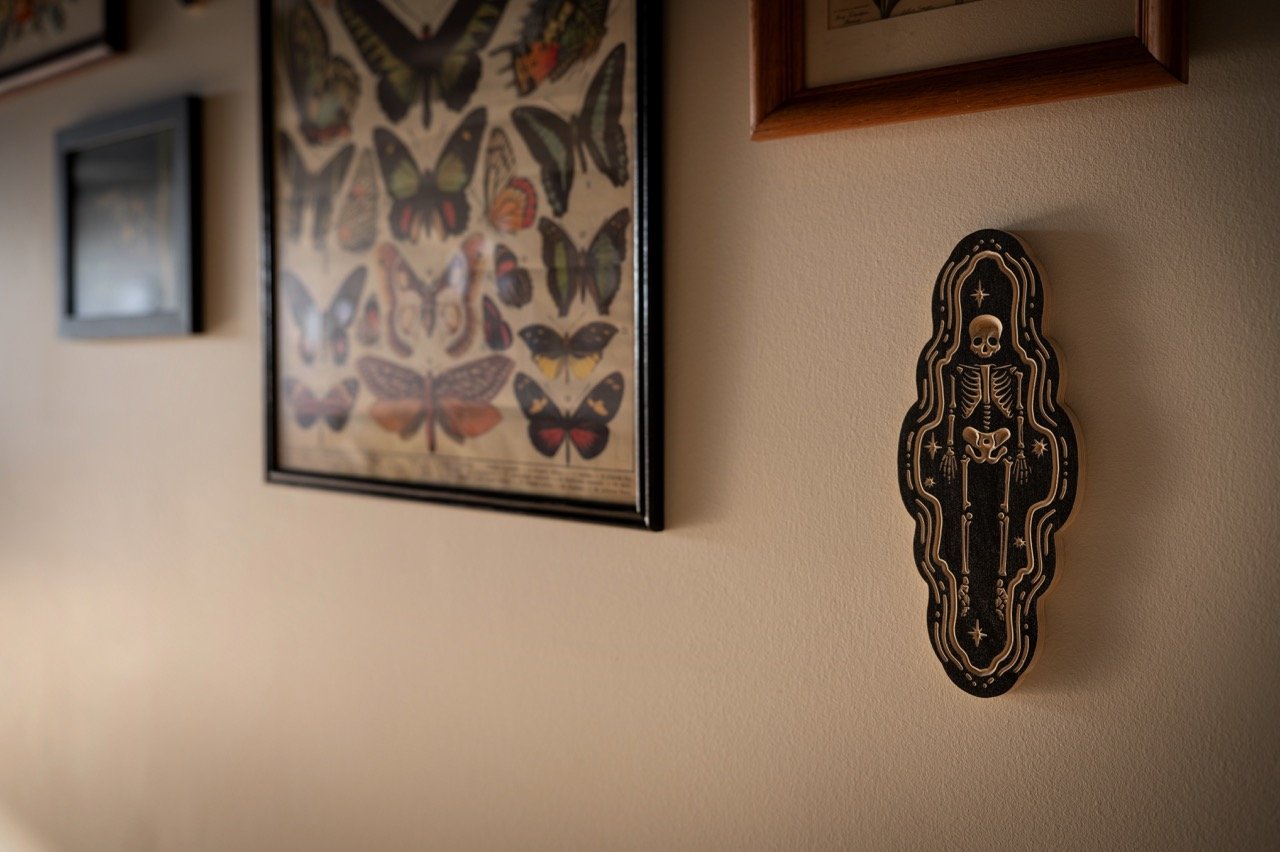Decorative wall art featuring a skeleton surrounded by stars and planetary symbols, with framed butterfly illustrations on the wall.