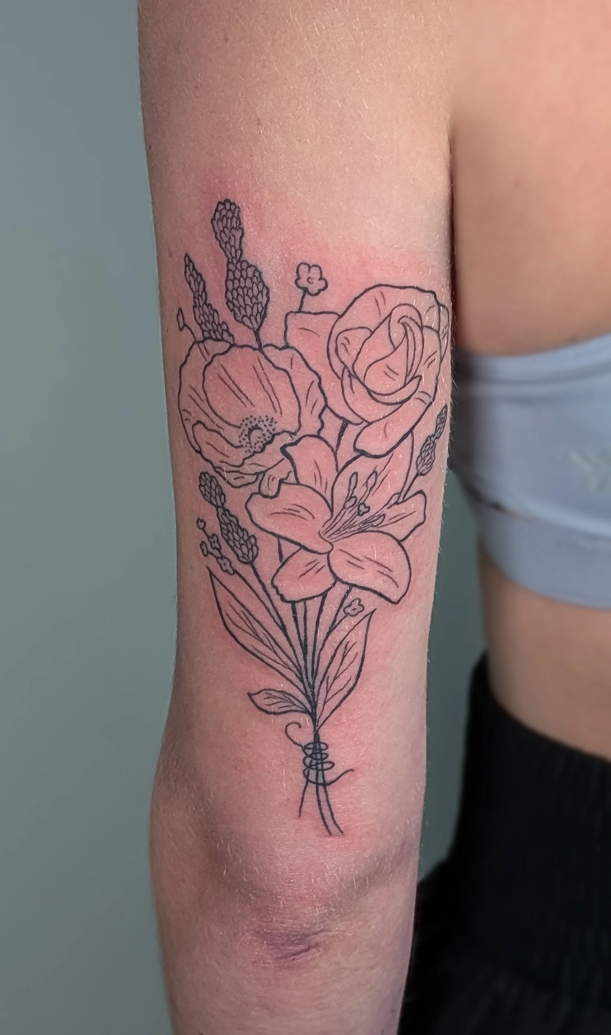 A tattoo of a bouquet of flowers with lilies, roses, and lavender on a person's forearm.