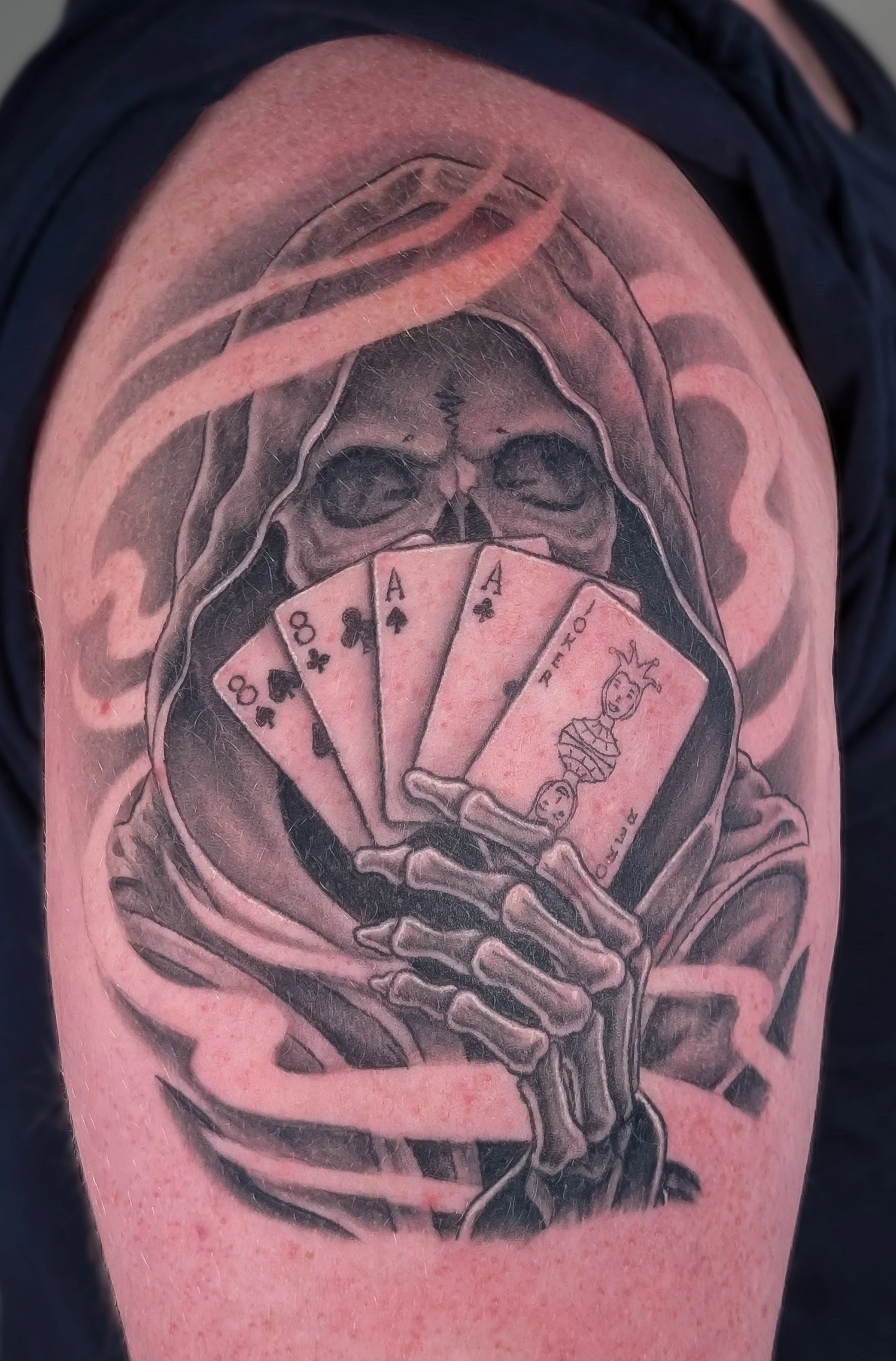 A striking black and grey tattoo of a reaper holding the Dead Man's Hand featured in the Billy the Kid lore.  The design features a swirling smoke background and high contrast elements.  Made by Caitie Brianna at Bone and Lily Tattoo in Knoxville, Te