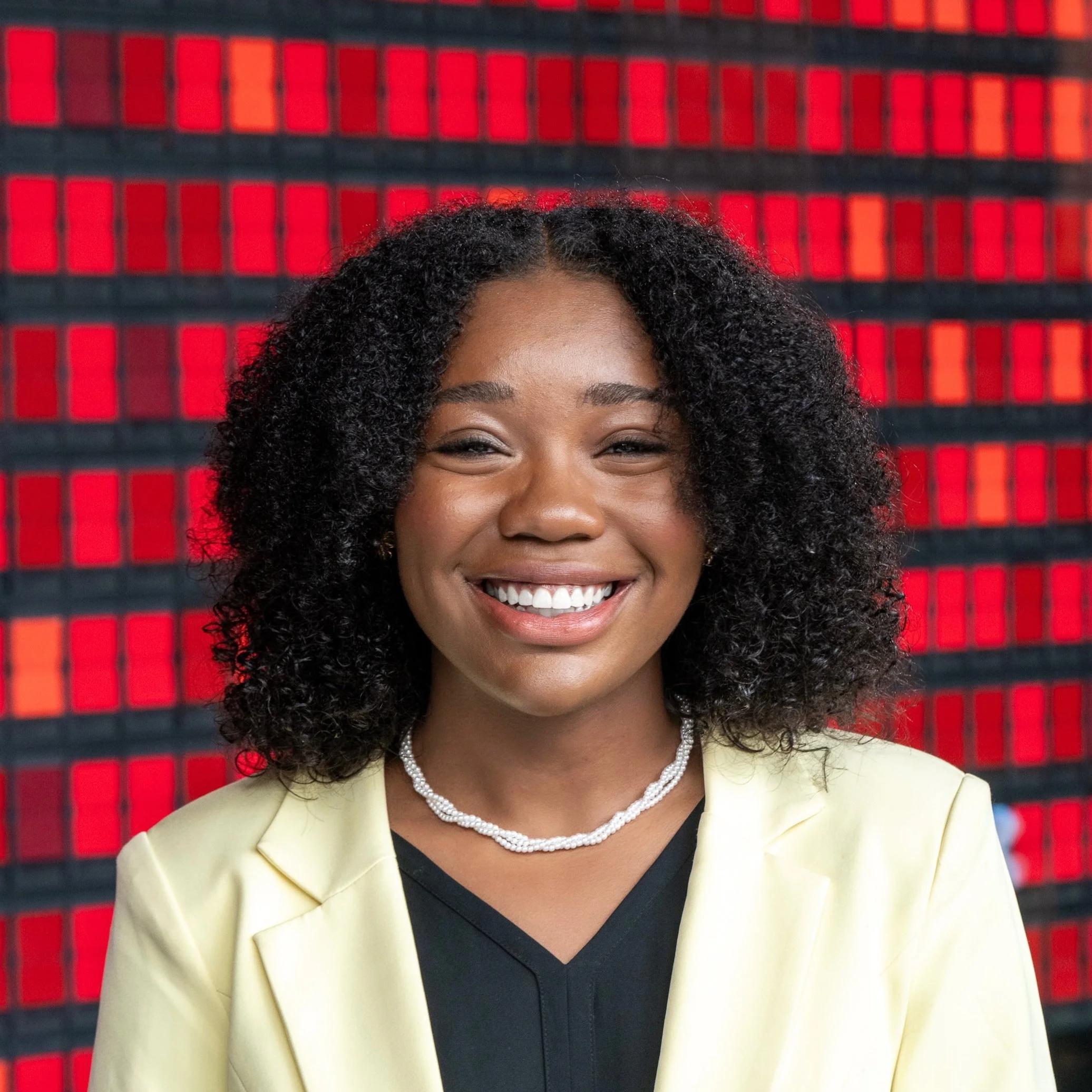 Smiling person with curly hair in front of a colorful background