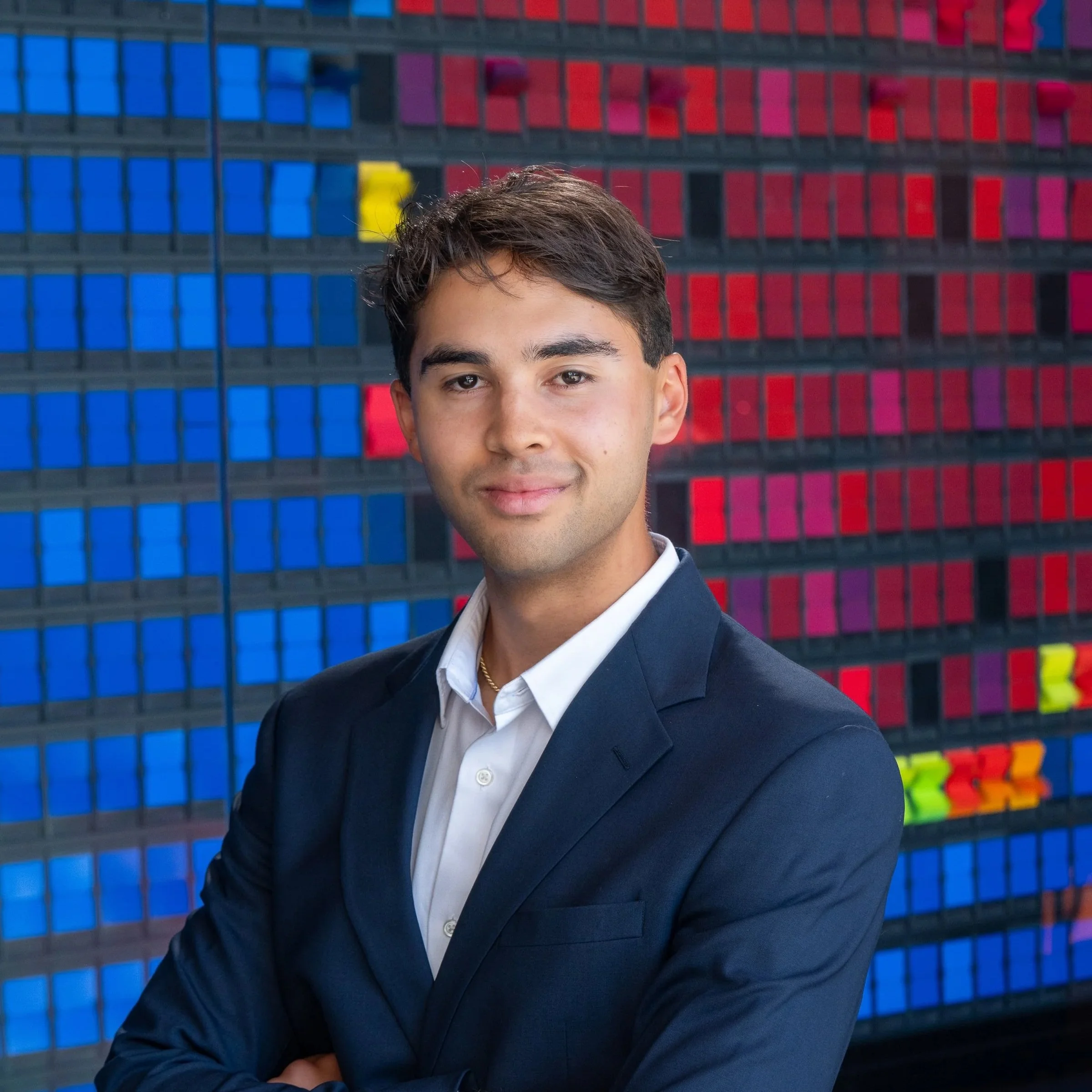 Smiling person with short hair in front of a colorful blurred background