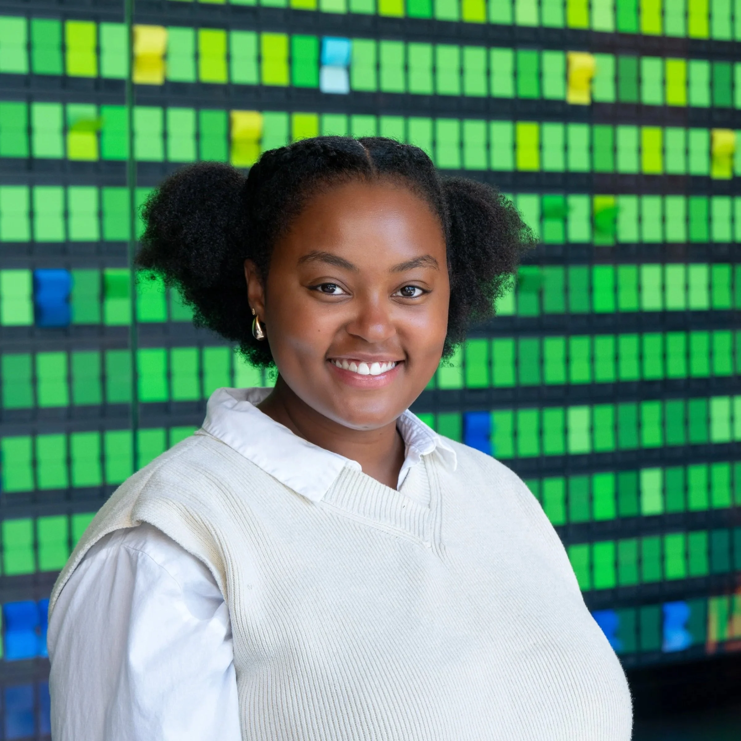 Smiling woman in red shirt with long black hair and large earrings in front of colorful background.