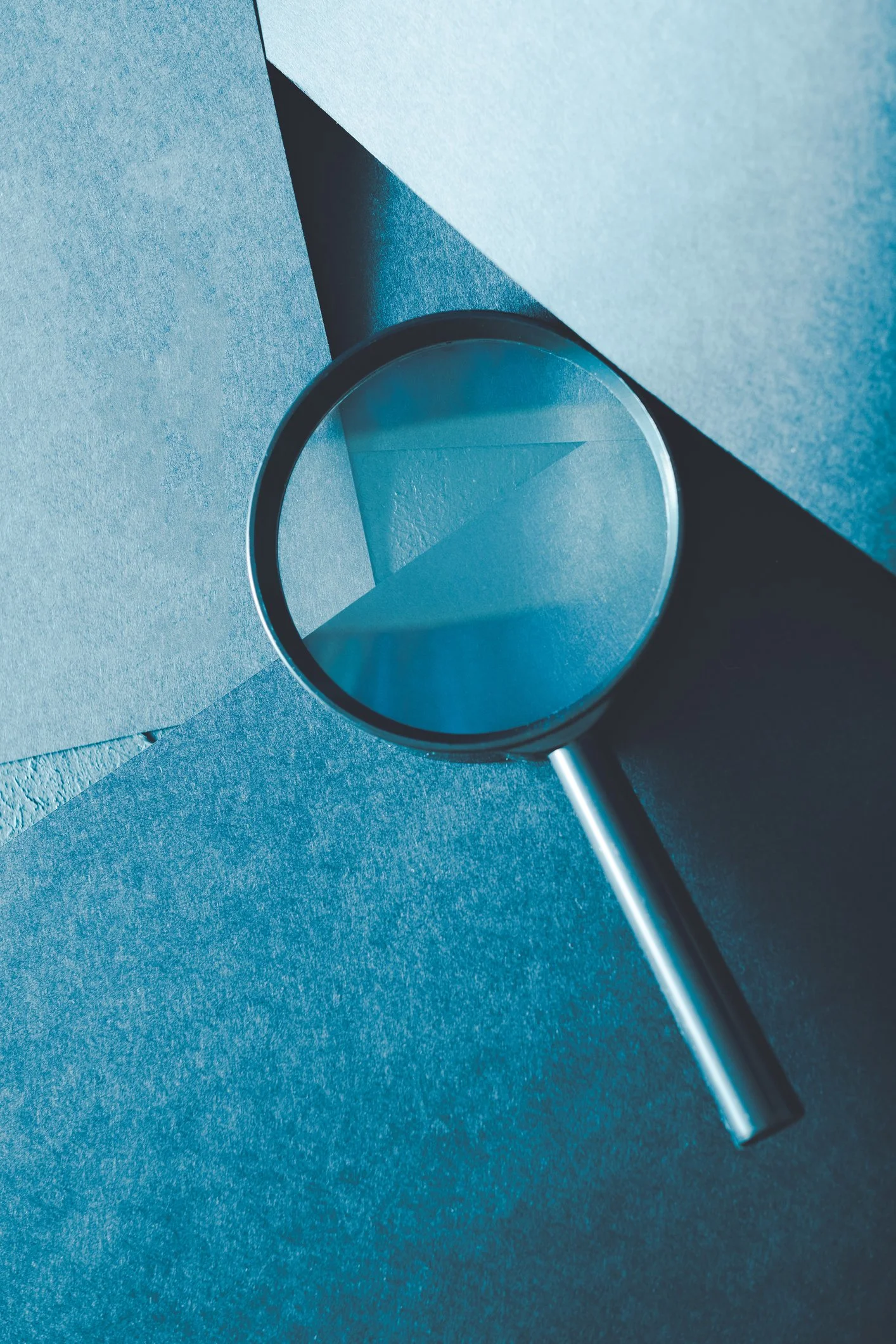 A mirror reflecting a blue sky with a cloud, mounted on a dark wall, illuminated by natural light.