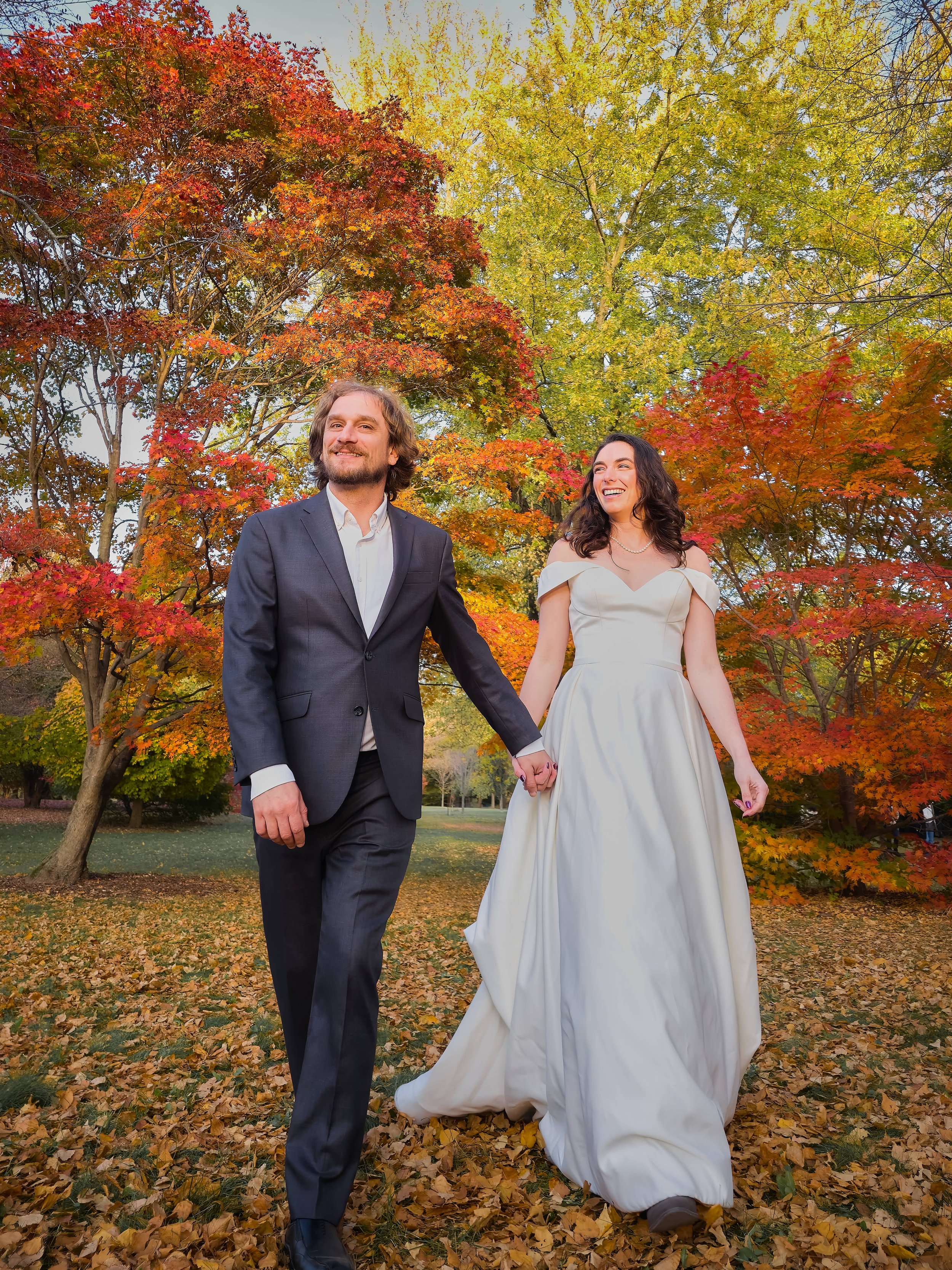 groom leads bride through autumnal forest photograph by Life Times Photography