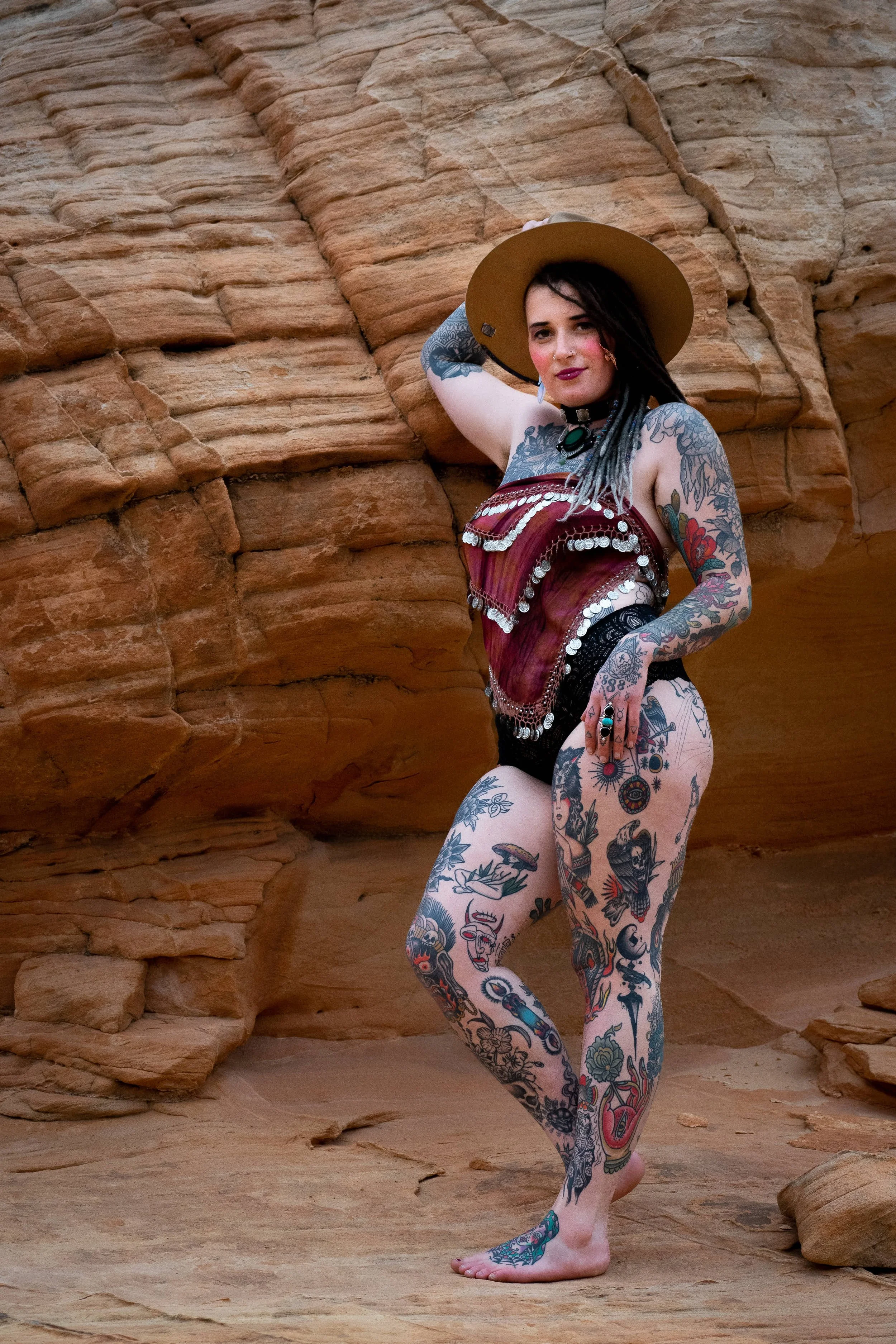 boho styled heavily tattooed model strikes sexy pose in rocky desert scene photograph by Life Times Photography