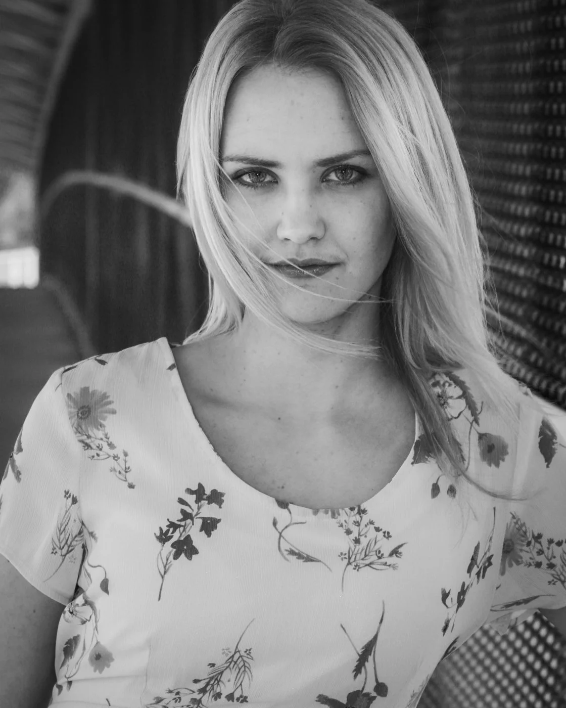 Black and white photograph of a young woman with shoulder-length hair, wearing a floral patterned top, looking directly at the camera with a subtle expression.