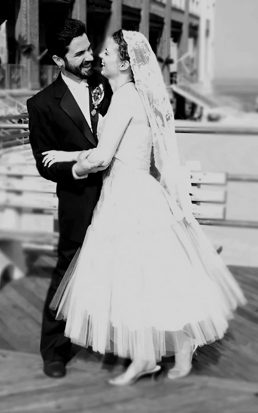 A black and white photo of a bride and groom dancing and smiling at each other on a wooden dance floor.