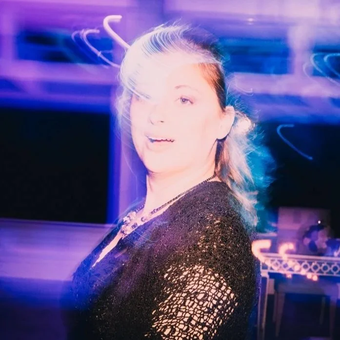 A woman with light hair and fair skin at a party or nightclub, with colorful lighting and motion blur effects showing movement.