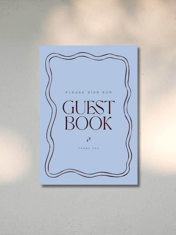Blue guest book sign with decorative border and text asking guests to sign, placed on a wall.