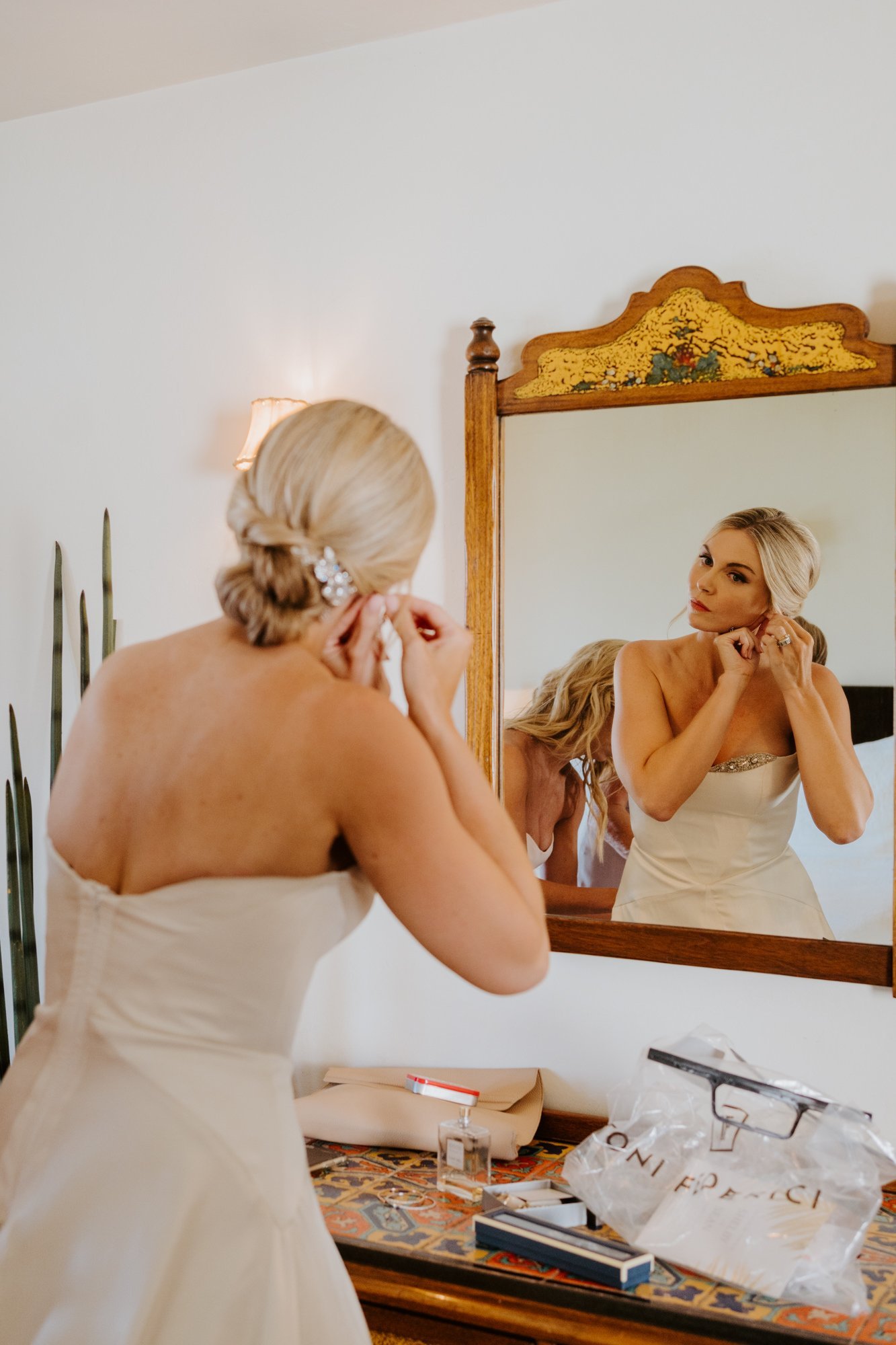 Bride putting on earrings, Elegant and classic low bun wedding hairstyle by Jen Plus Colour in Palm Springs, photography by Tida Svy