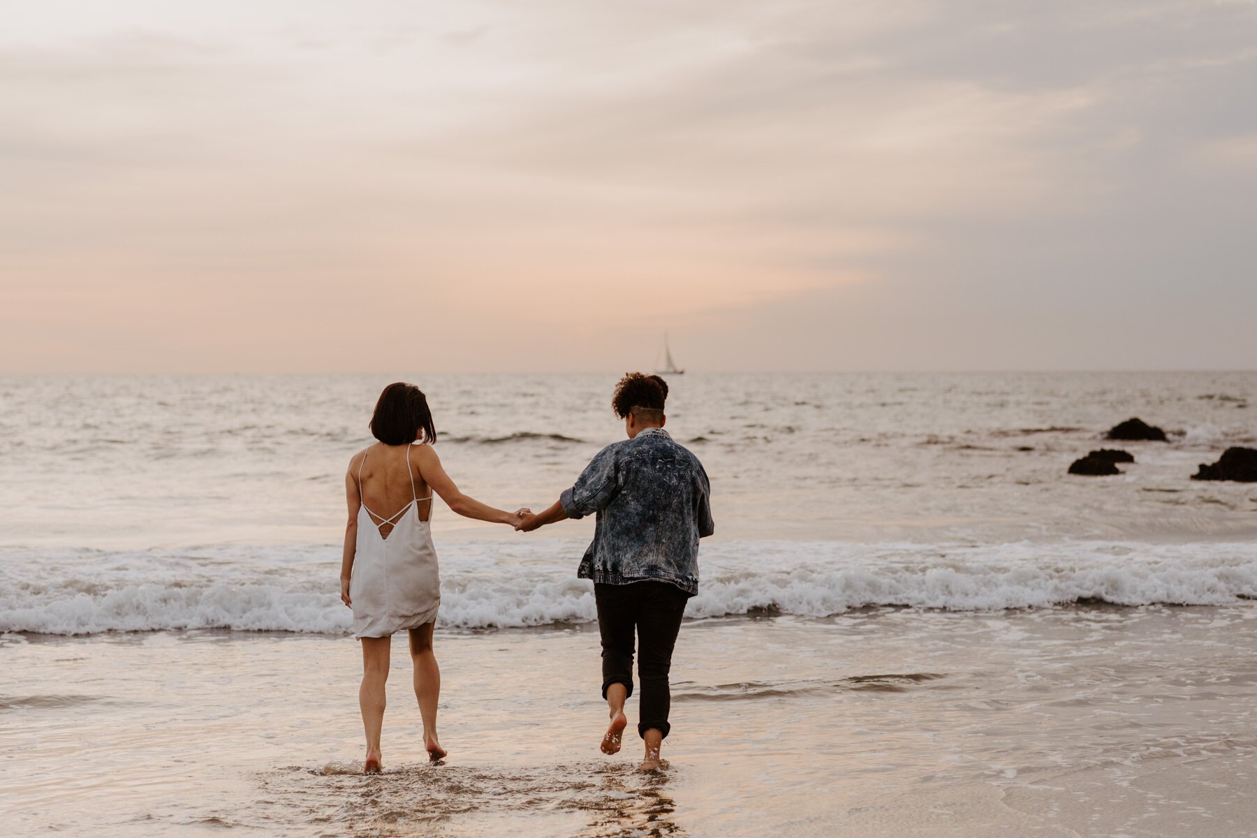Lesbian couple holding hands walking into the ocean at their Venice Beach engagement session
