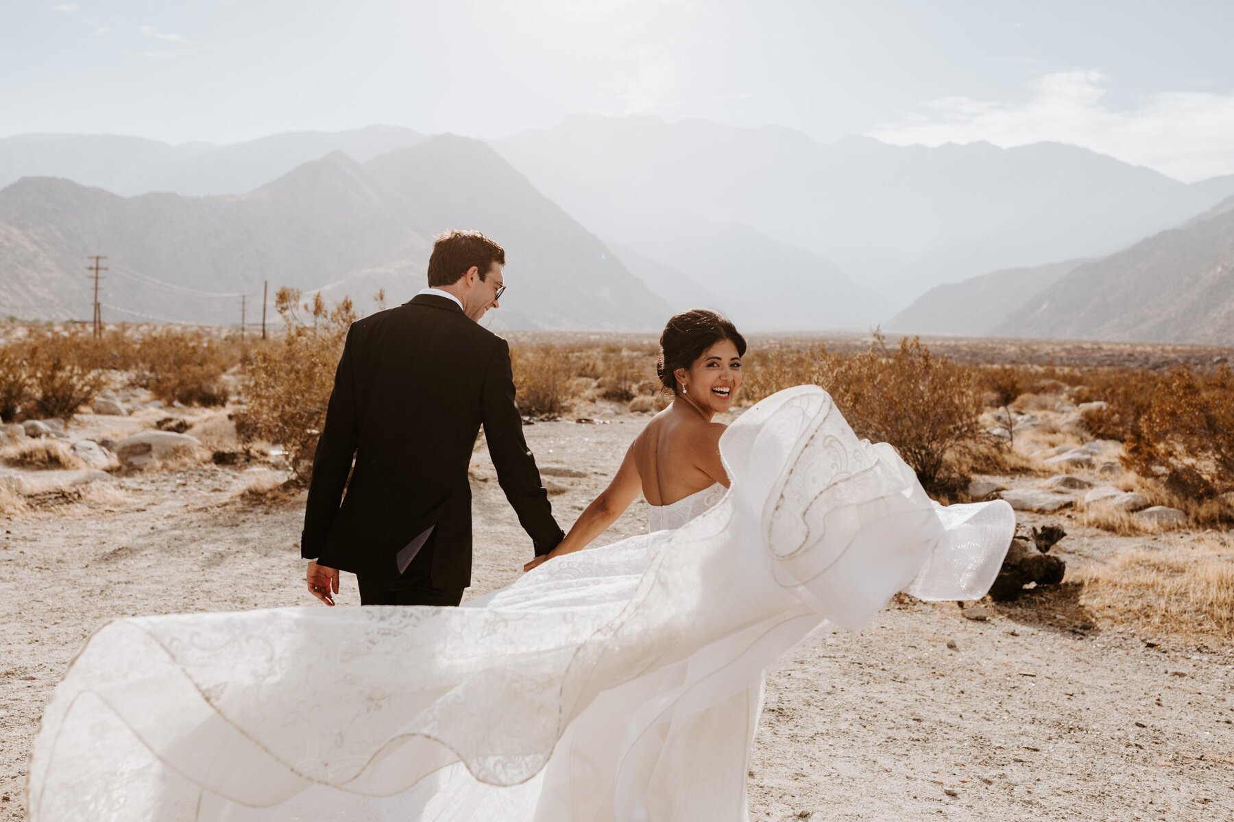 Bride and Groom running into the desert, wedding dress flowing, Palm Springs Wedding and Elopement Photographer, Photo by Tida Svy