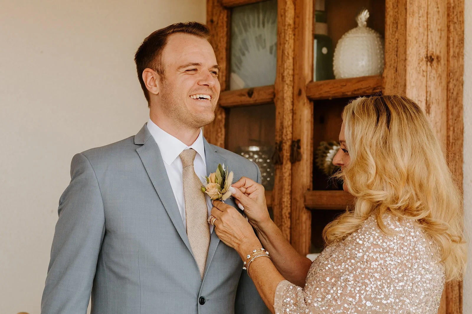 Mother of the bride pinning boutonniere on groom in blue suit, smiling and happy, groom getting ready, Rancho Palos Verdes backyard wedding, Photo by Tida Svy