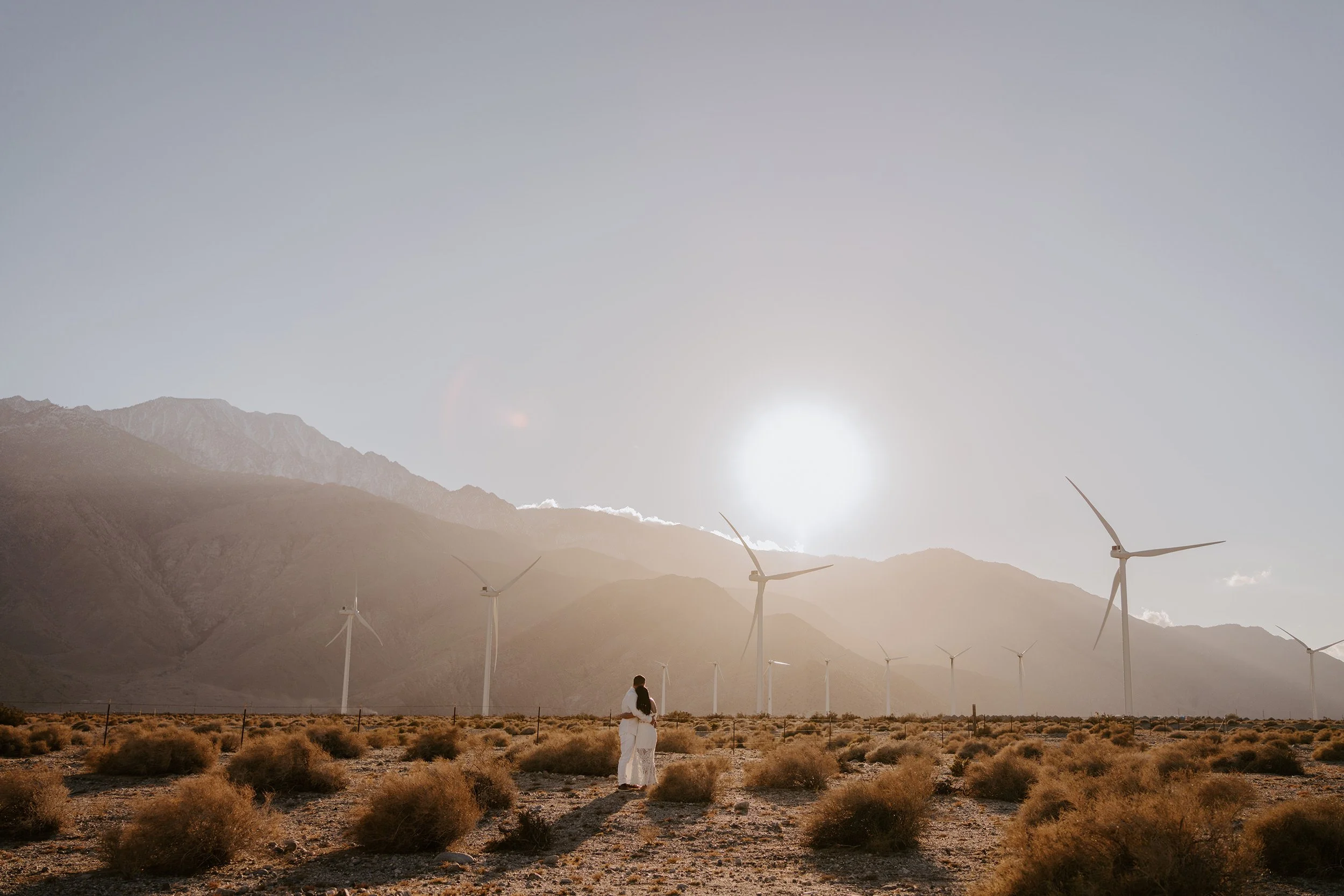 Couple embracing at sunset at the Palm Springs windmills during golden hour wedding portraits by Tida Svy