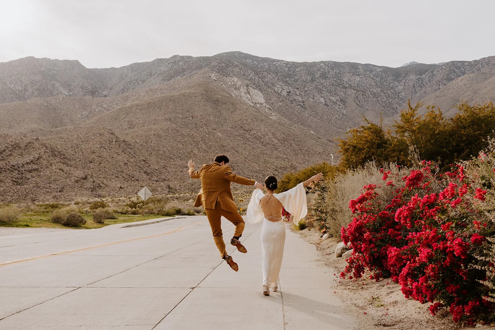 Wedding holding hands and walking towards mountains at sunset in Palm Springs.