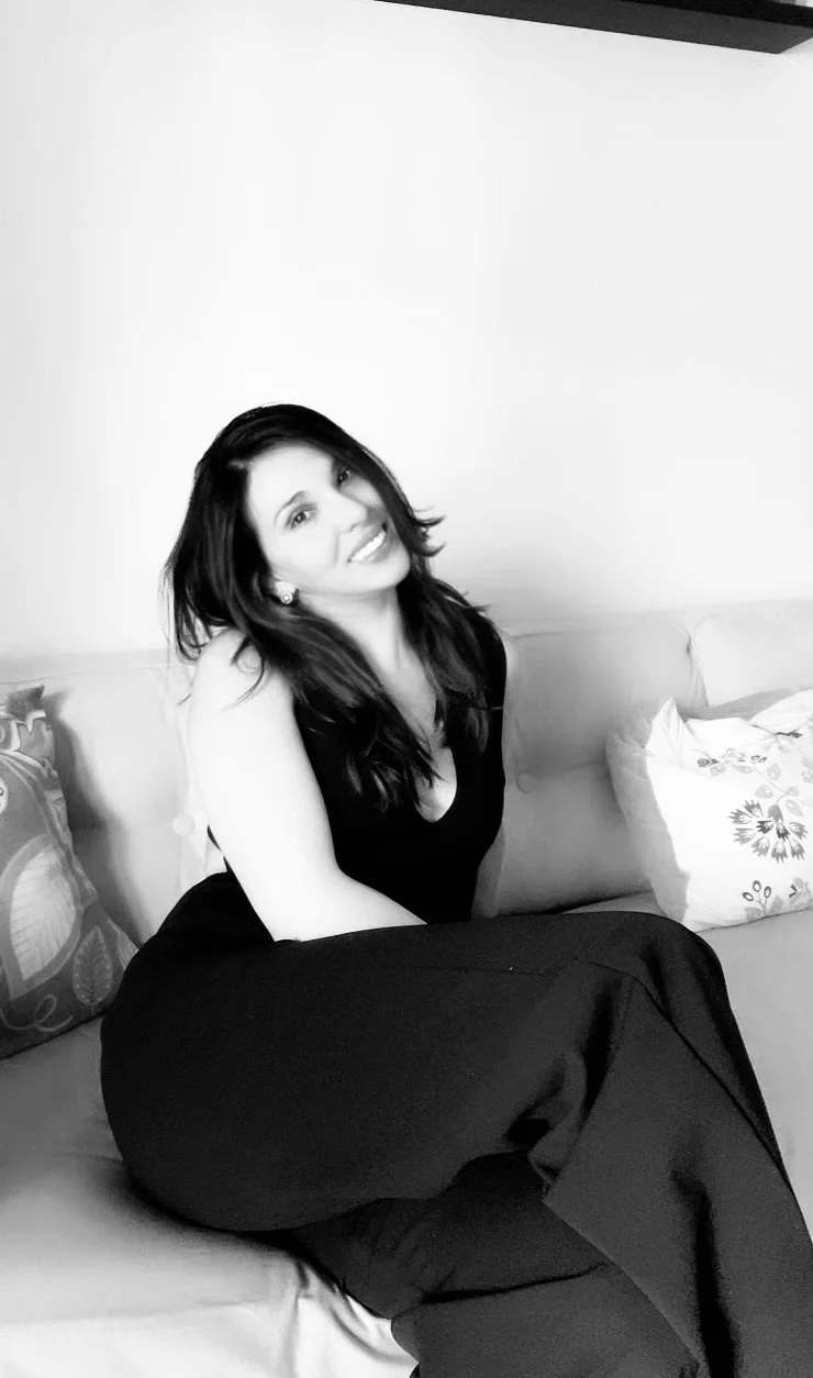 Smiling woman with long hair sitting on a couch with decorative pillows, black and white photo.