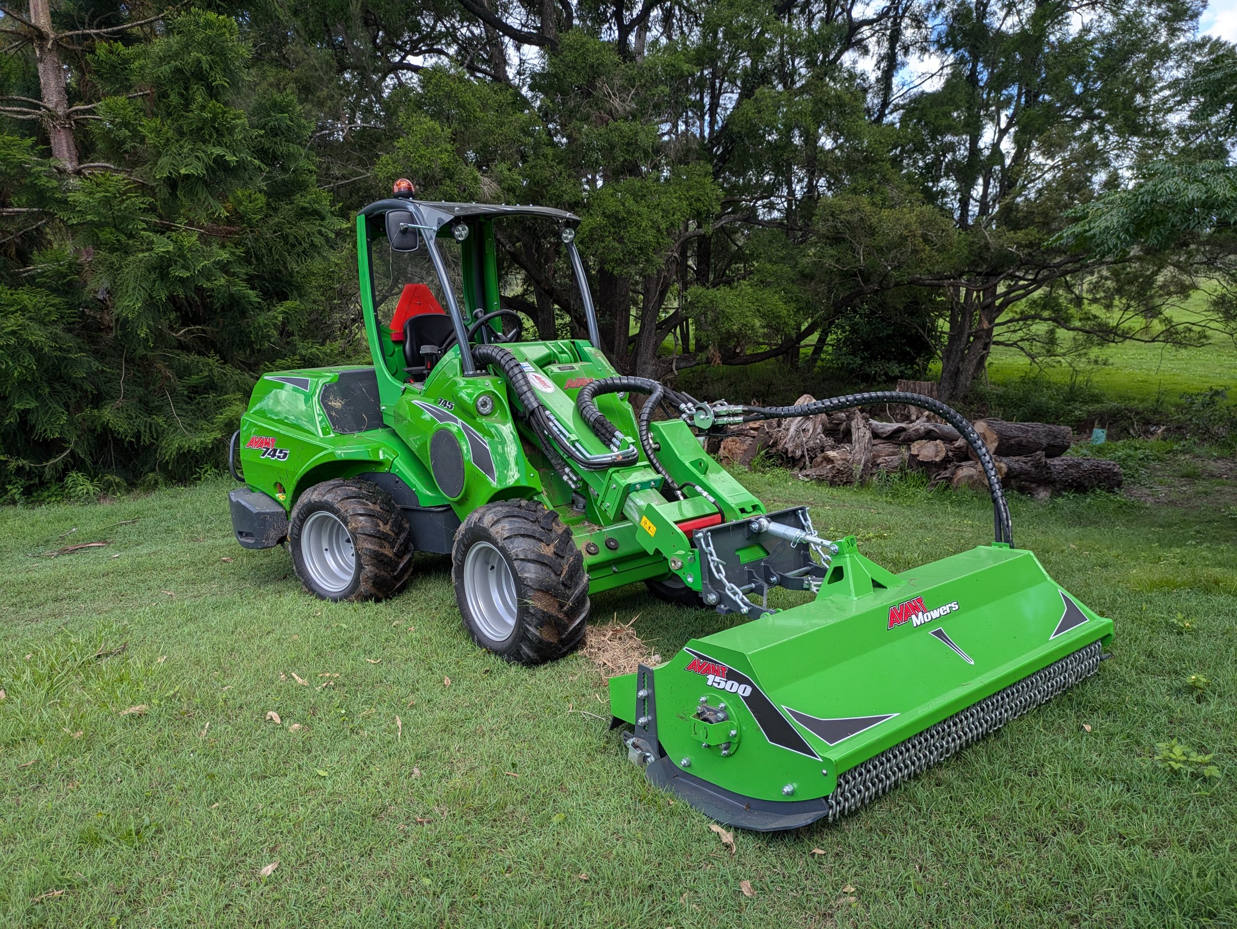 Green Avant 745 Loader with 1500mm flail mower attachement parked next to sensitive environmental creek system ready to control invasive vines and woody weeds like lantana