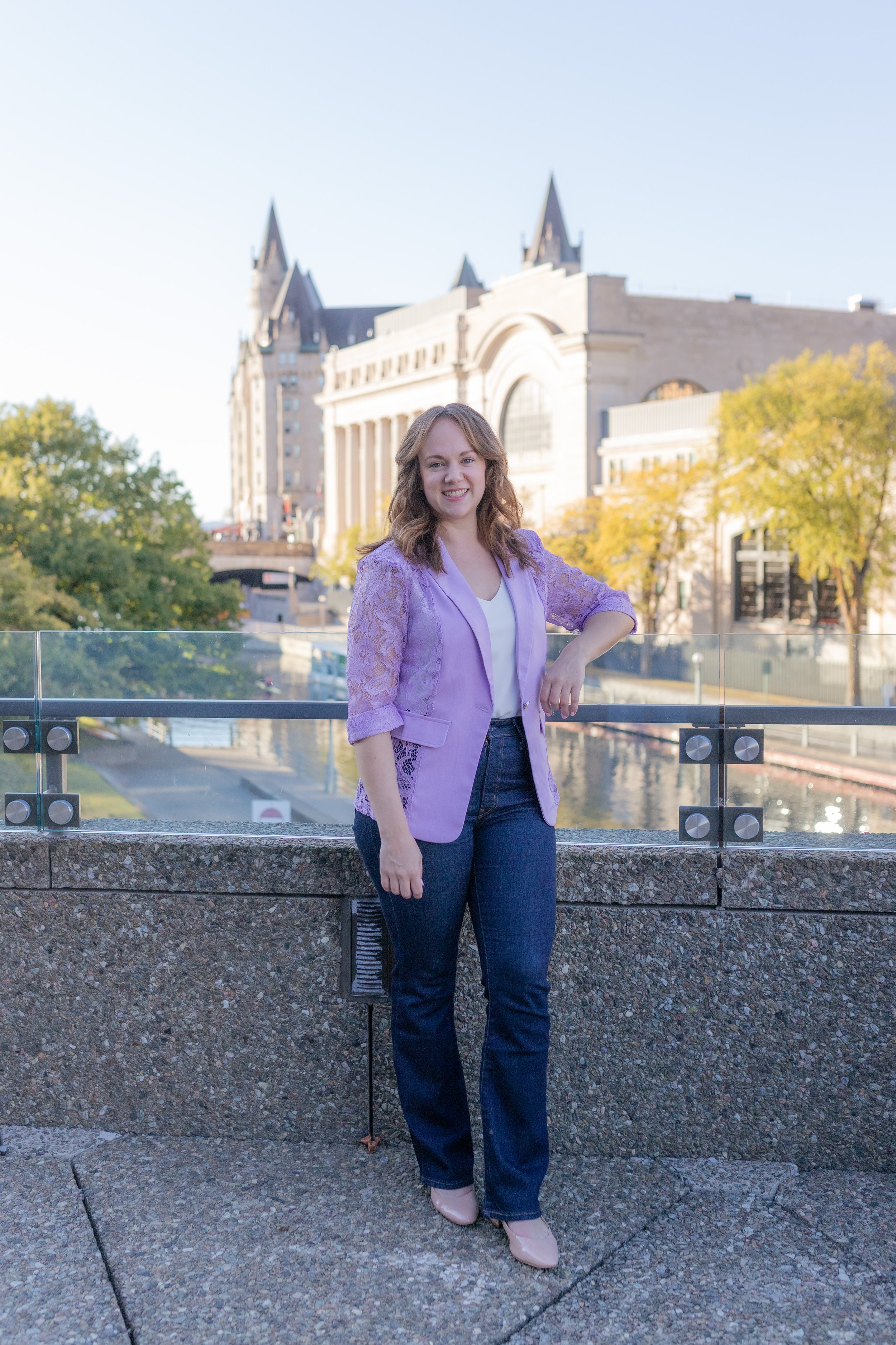 Nina Nesdoly standing on a balcony in a purple jacket, smiling towards the camera.