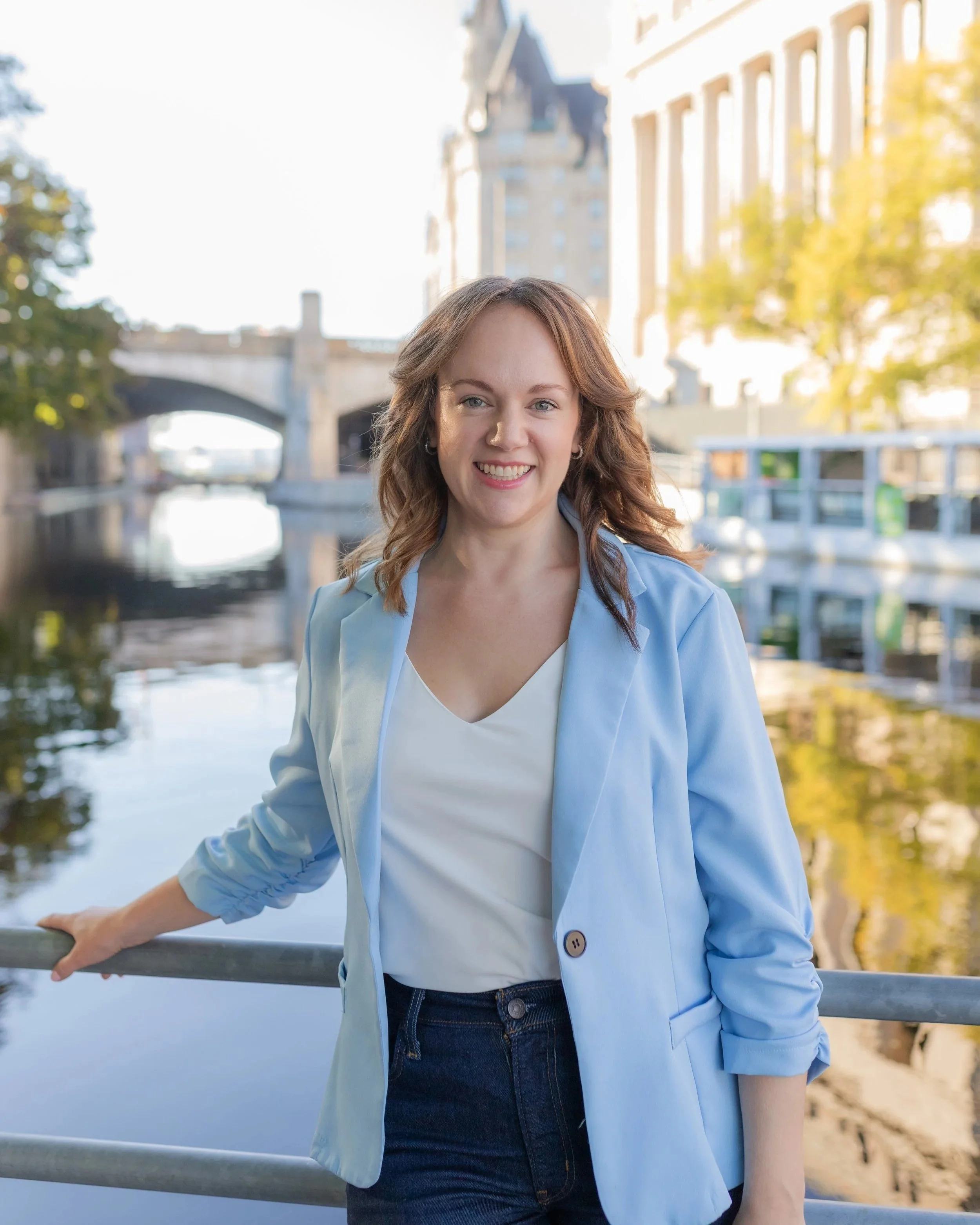 Nina Nesdoly standing by a canal in a blue jacket, smiling towards the camera.